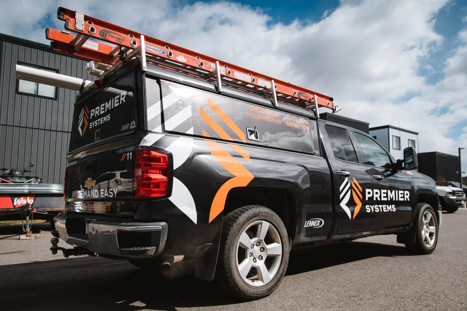Premier Systems black Chevy truck wrap with bold orange and white angular graphics, ladder rack, and business branding for HVAC services. A custom commercial vehicle wrap for a service fleet in Bozeman, Montana.