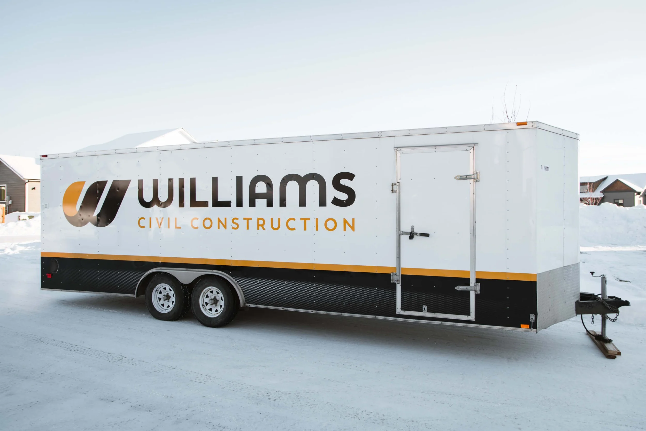 Williams Civil Construction trailer wrap in Bozeman, Montana, in a clean white and black color palette with bold orange accents and large logo placement on the driver side. 