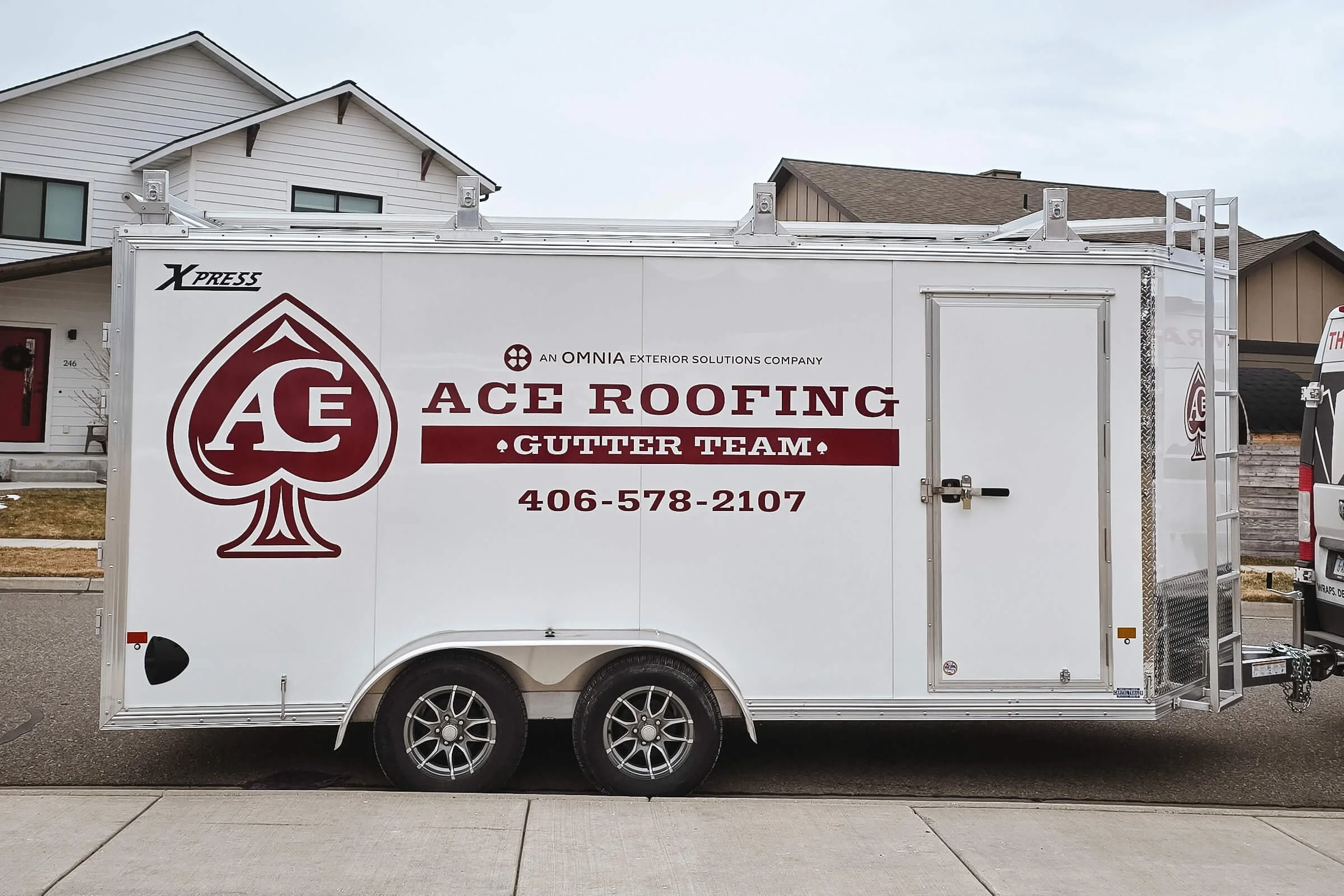 Ace Roofing trailer graphics in Bozeman, Montana, featuring burgundy logo and ace of spades design on a white trailer with simple text showcasing the company’s name and phone number.