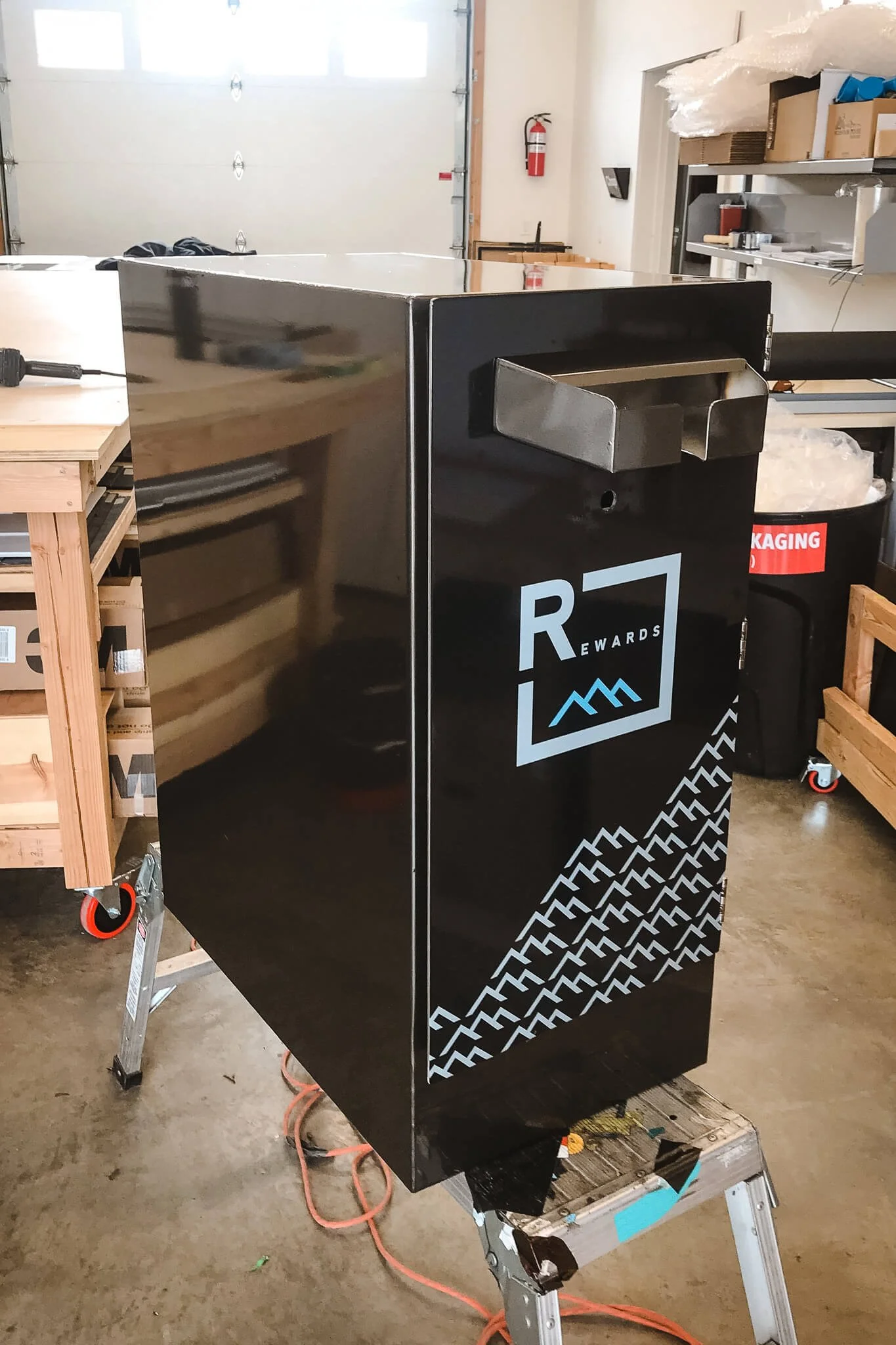 Custom black cabinet wrapped in glossy vinyl with the R+Rewards logo and mountain pattern in light blue, demonstrating the branding capabilities of custom vinyl wraps.