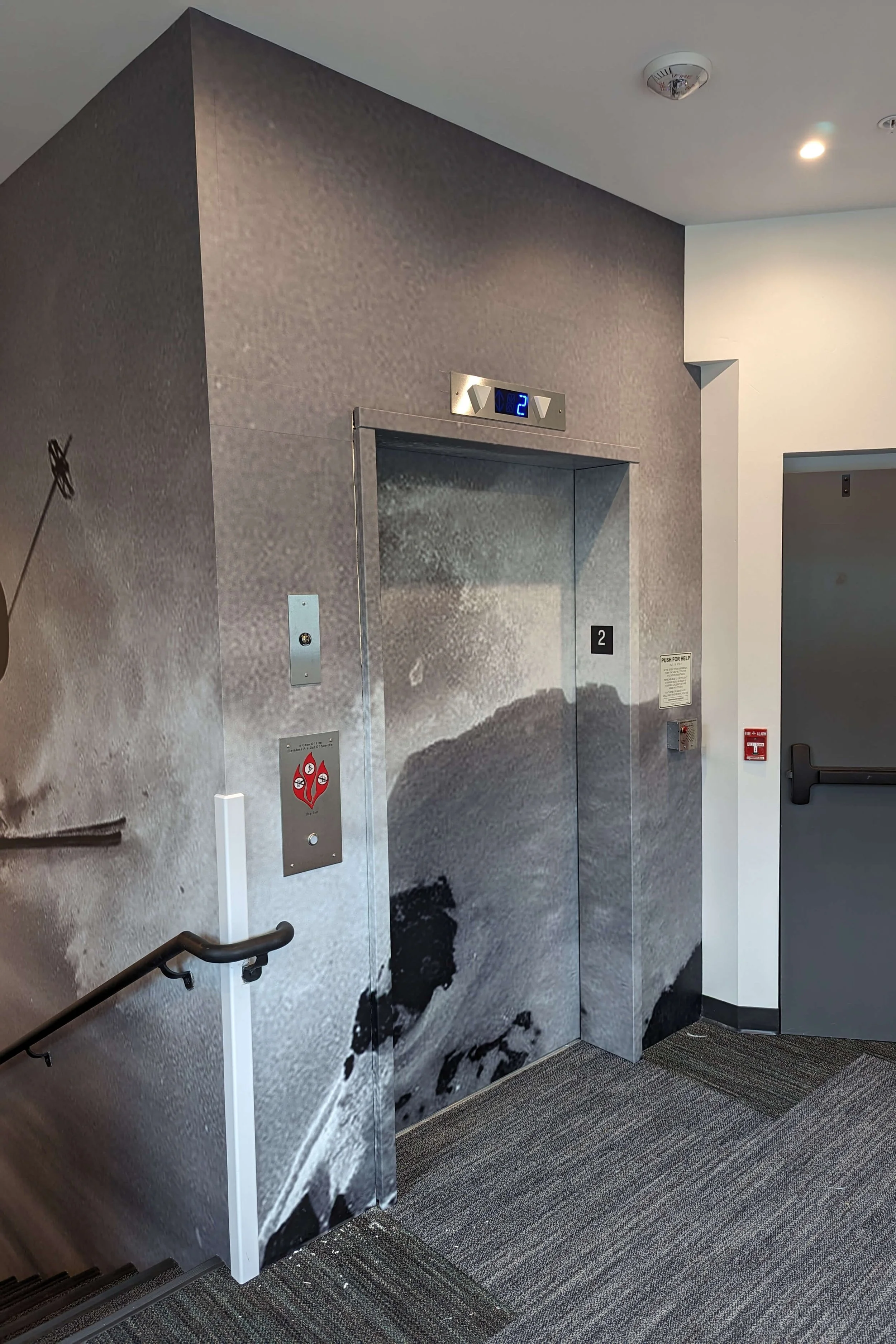 Contemporary elevator lobby with a grayscale ski scene wall wrap spanning the walls and elevator doors for a cohesive design. Location: Big Sky, MT.