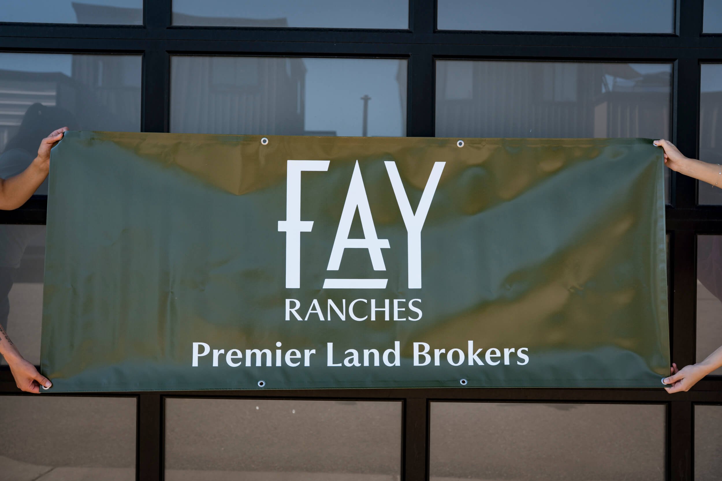 Dark green vinyl banner with silver grommets showcasing a white Fay Ranches Premier Land Brokers logo