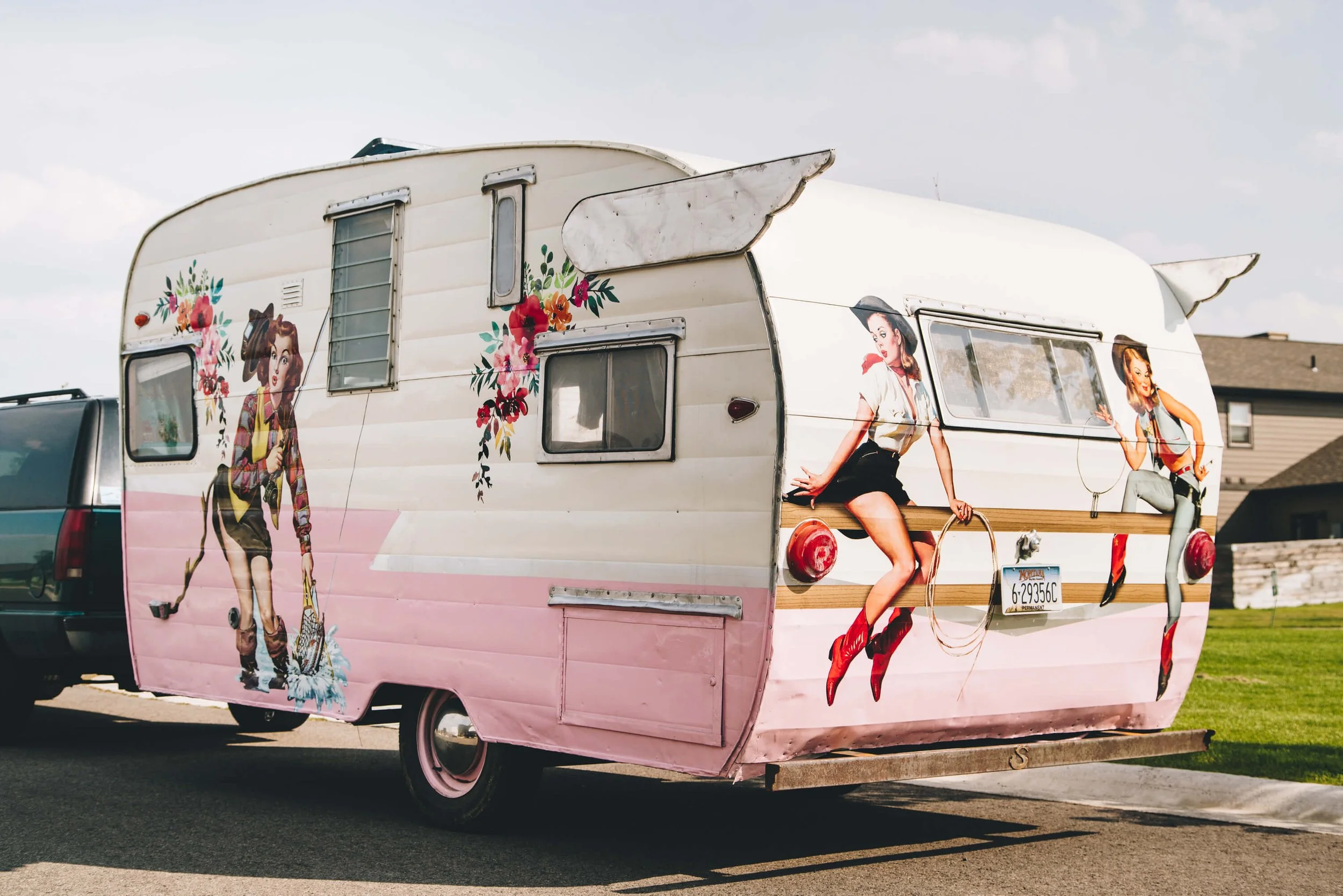 Full custom trailer graphics on a vintage camper with multiple retro cowgirl illustrations and floral accents, blending pastel pink and cream striping for a nostalgic look.