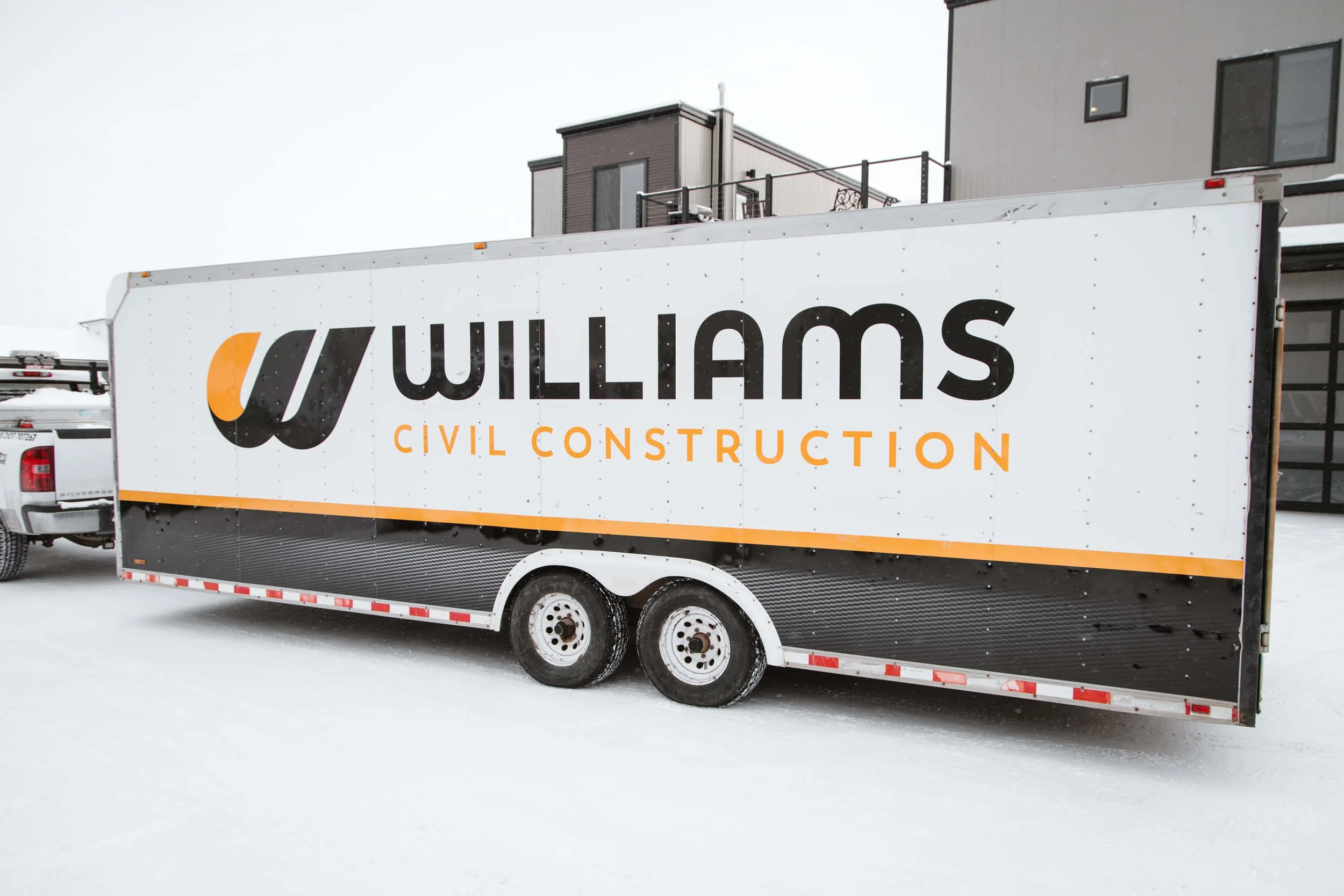 Williams Civil Construction trailer graphics in Bozeman, Montana, with a sleek black-and-white wrap and bold yellow accents, emphasizing brand strength and road visibility.