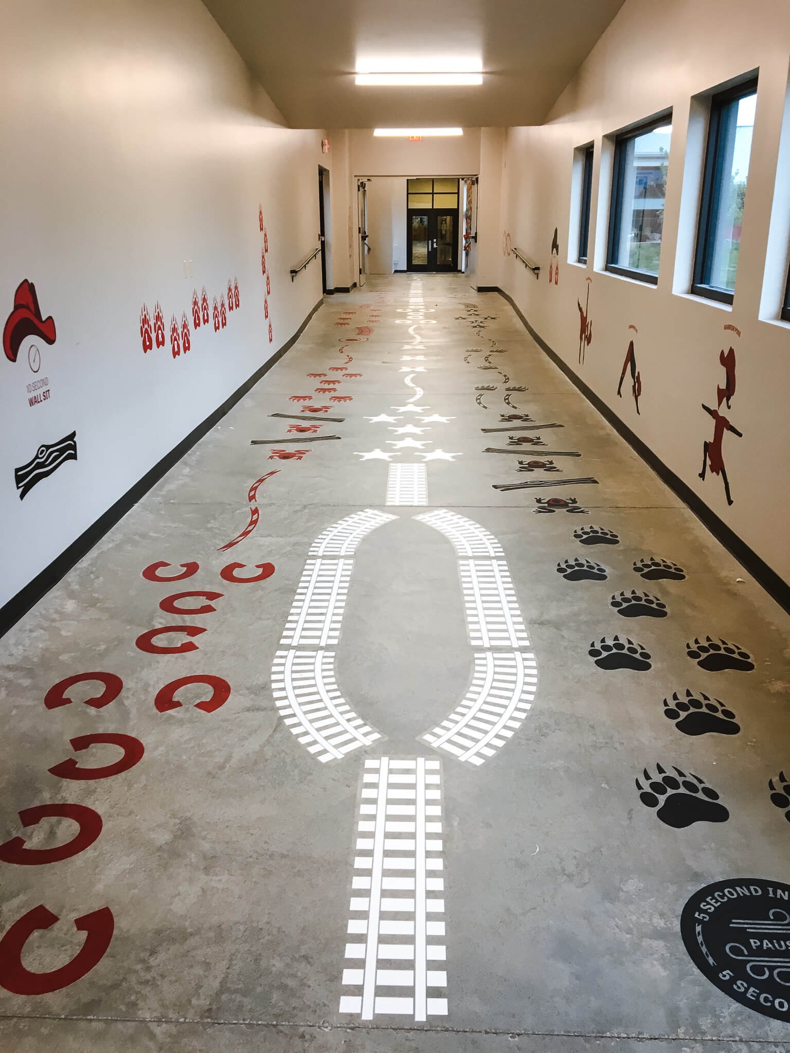 Elementary school hallway enhanced with custom vinyl wraps depicting railroad tracks, bear tracks, and directional graphics to engage students and guide foot traffic.