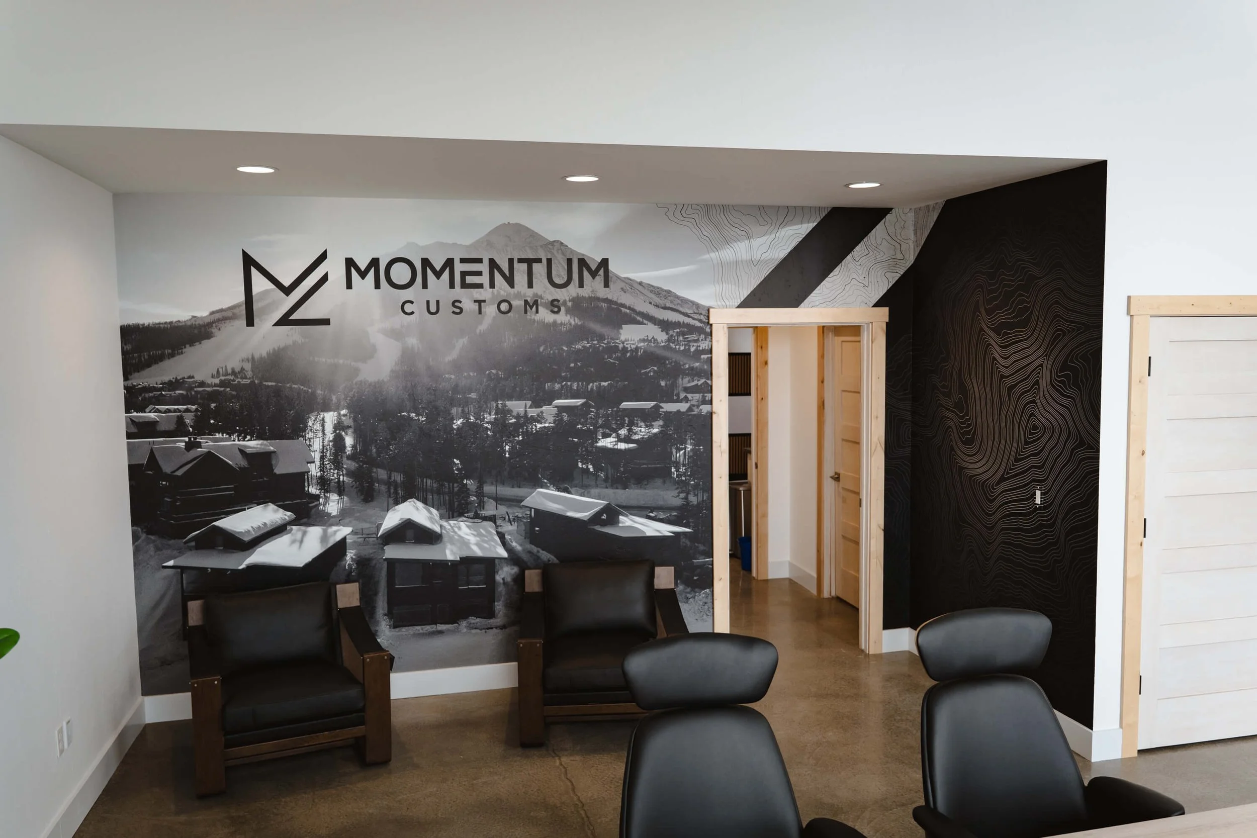 Black and white custom wall wrap with mountain and ski run imagery, incorporating the Momentum Customs logo in a sleek, modern office setting at Momentum Customs in Bozeman, MT.