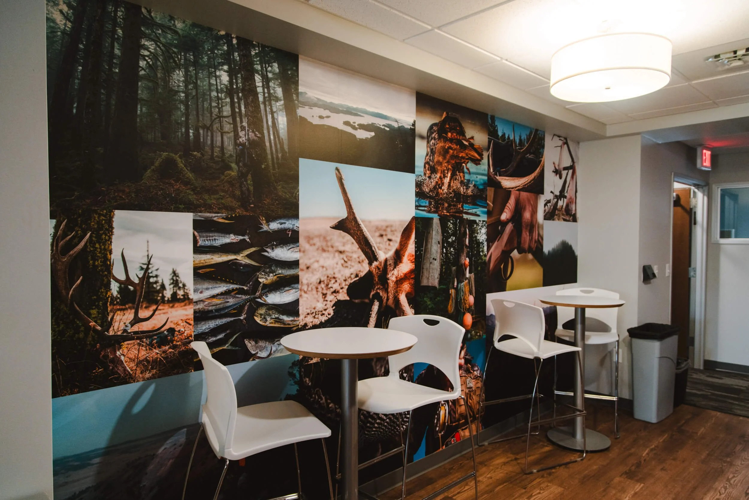 Office breakroom hallway featuring a wall wrap collage of outdoor and wildlife photos of trees, fish, and antlers, creating custom wall graphics that bring nature indoors. Location: MeatEater, Bozeman, MT.