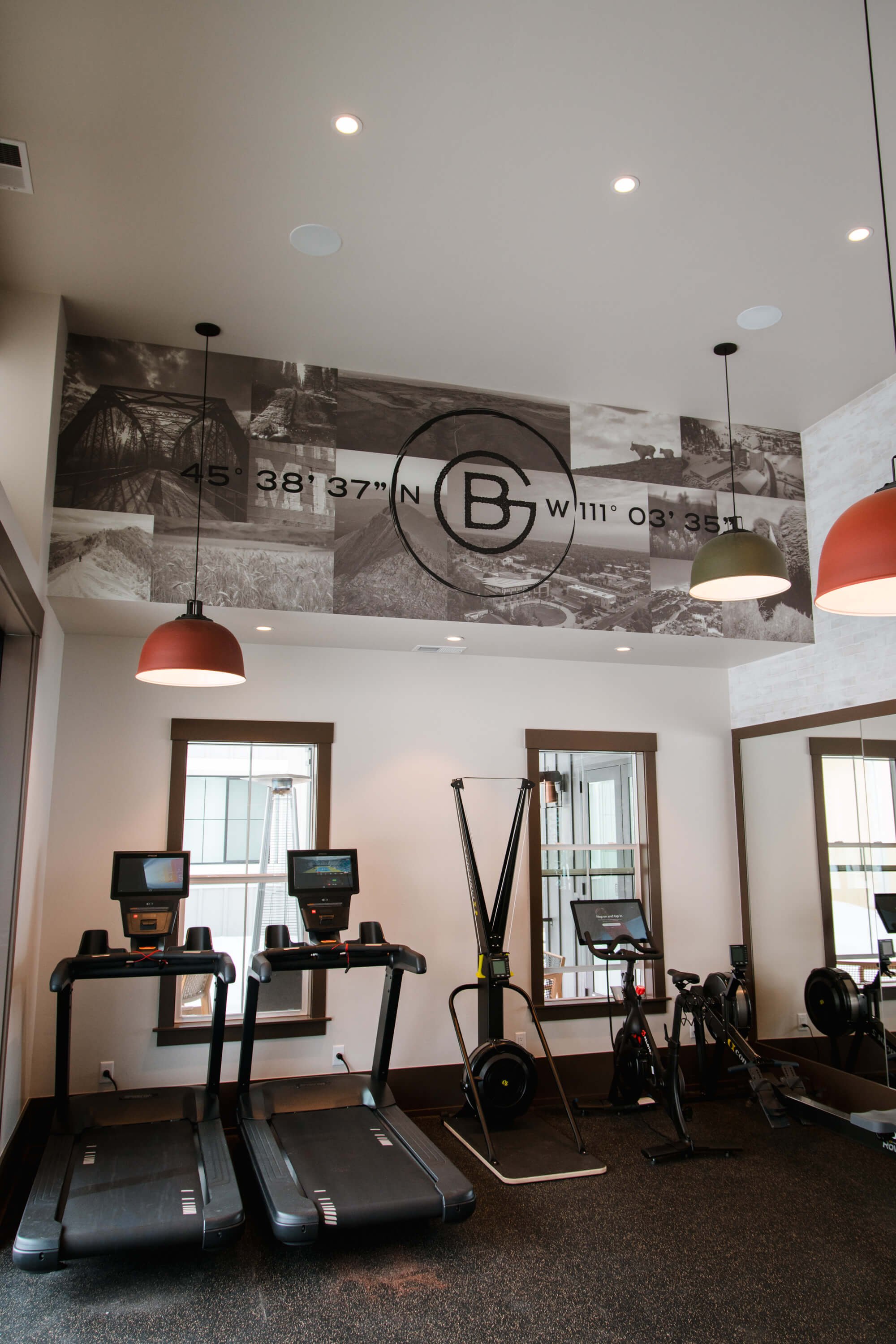 Ceiling-mounted wall wrap with black-and-white photography collage and custom coordinates with bold "B" branding in a gym cardio room. Installed by The Wrap Agency at Blackwood Groves.