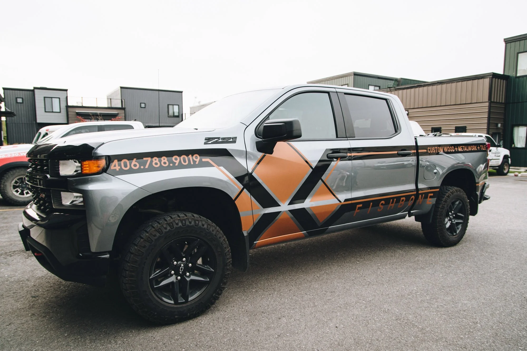 Custom truck wrap for Fishbone featuring striking geometric design in orange, gray, and black with business contact info and services displayed—a standout fleet graphics solution in Bozeman, Montana.