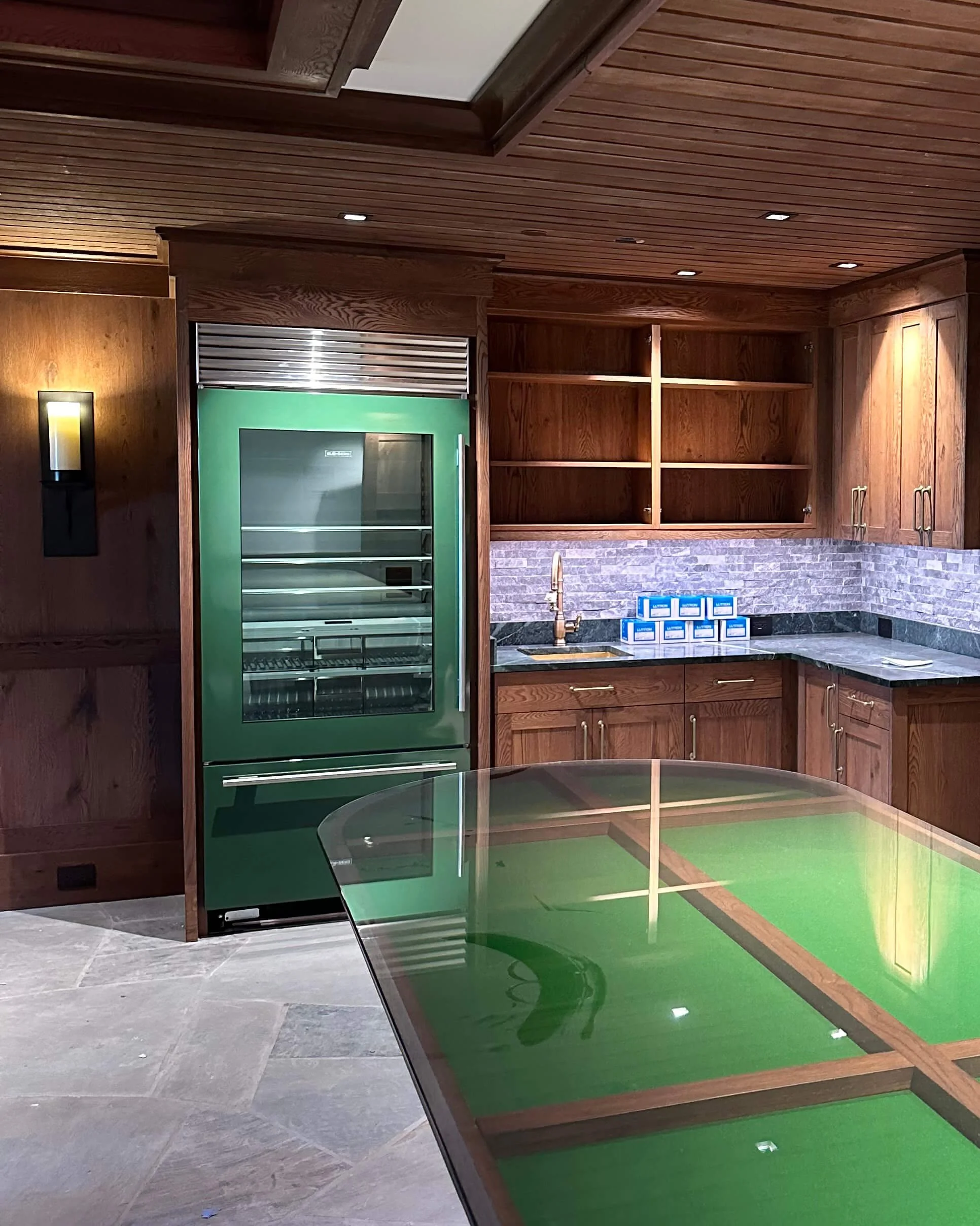 High-end kitchen with dark cabinetry and stone counters and backsplash, features a green partial wrap on the front of the refrigerator.