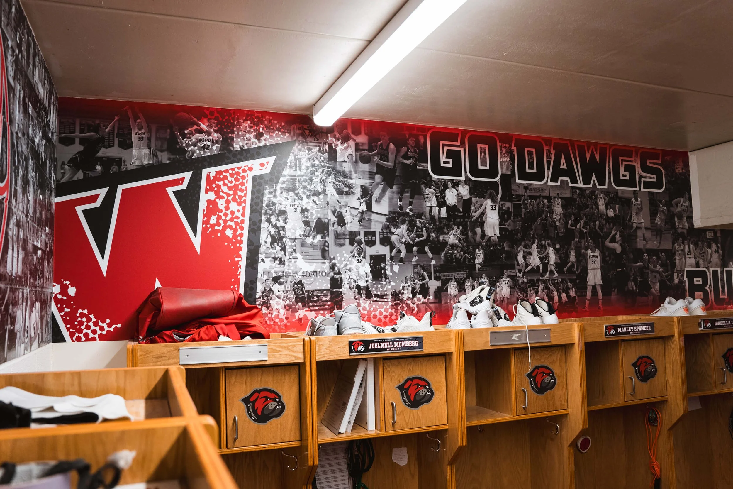 Bold red and black sports wall wrap for a locker room, featuring action-packed photo collage of basketball players, a large “W” lettermark, and the phrase “Go Dawgs.” Business Location: UM Western in Dillon, MT.