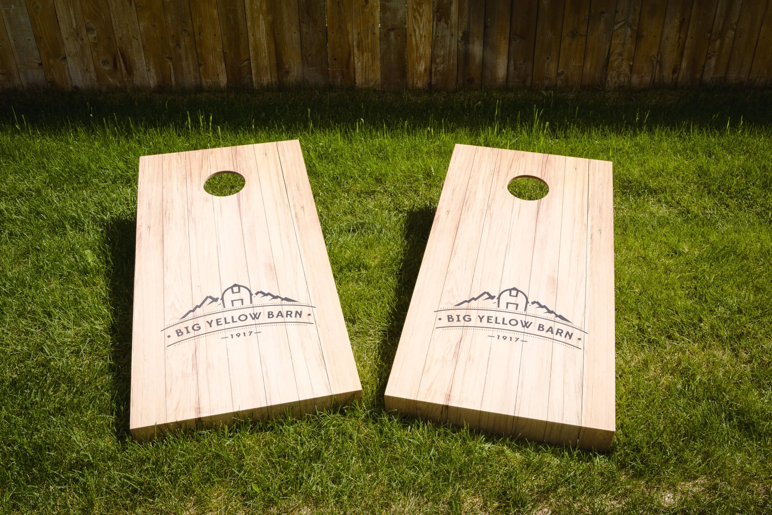 Custom vinyl wraps applied to a pair of cornhole boards featuring the Big Yellow Barn logo, designed to enhance branding with natural woodgrain aesthetics.