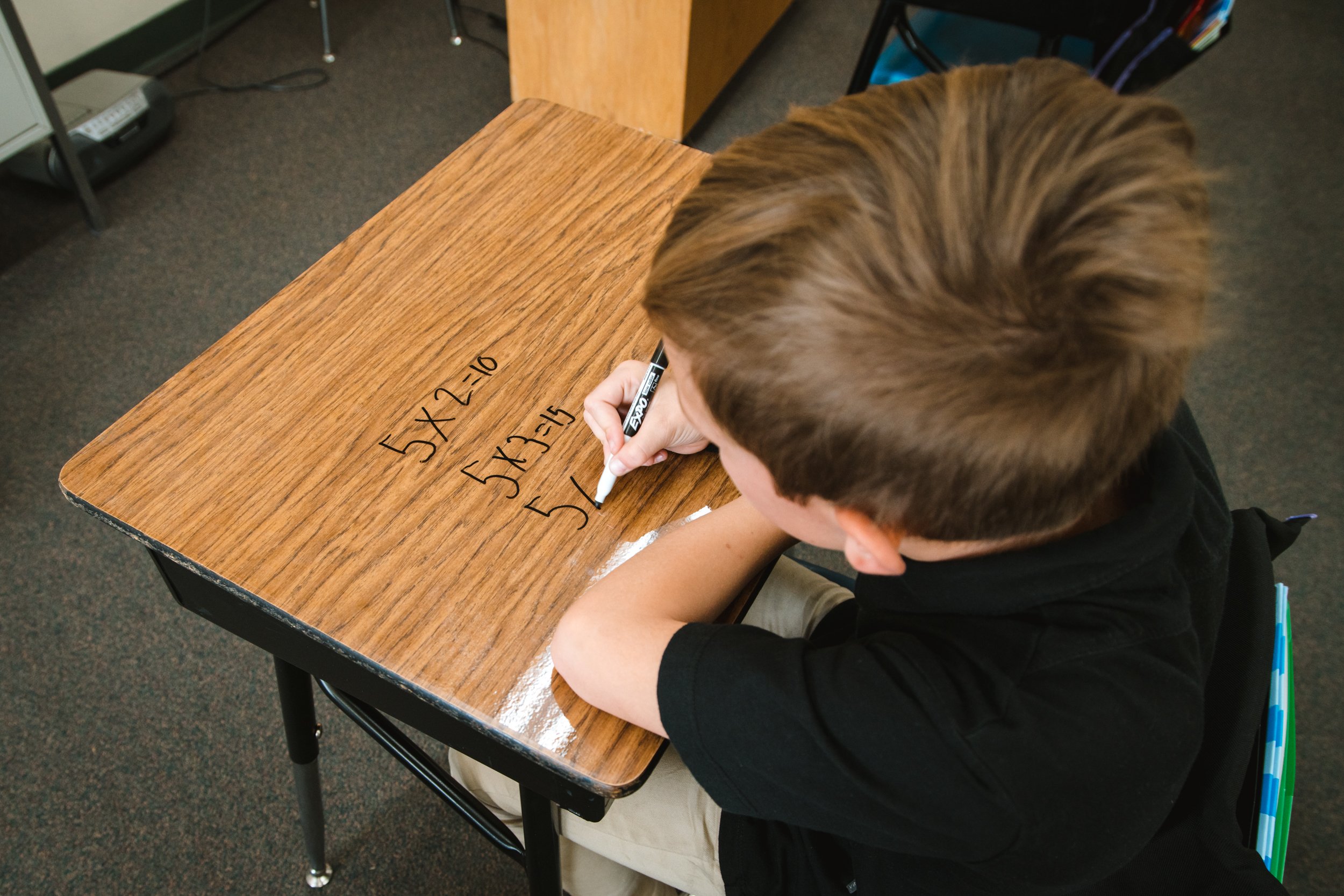 Student practicing multiplication directly on a classroom desk with a dry erase surface.