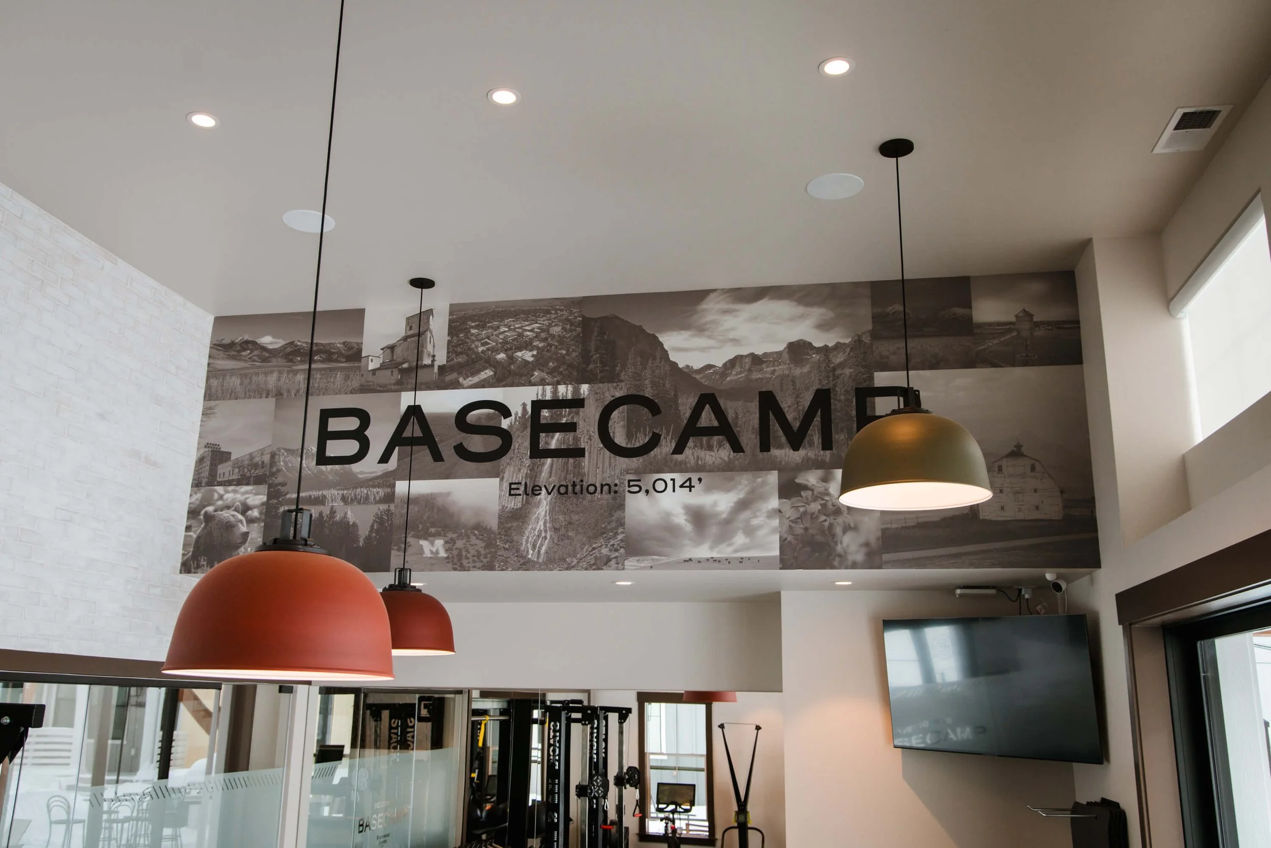 Large-scale wall wrap reading "BASECAMP Elevation: 5,014'" with grayscale landscape collage in a modern fitness center. Installed by The Wrap Agency at Blackwood Groves.
