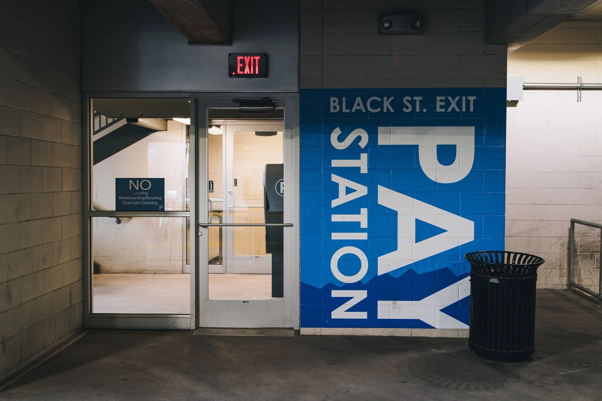 Bold blue directional wall wrap reading “PAY STATION” with clear typography guiding visitors near the Black Street exit of a parking garage in Bozeman, MT.
