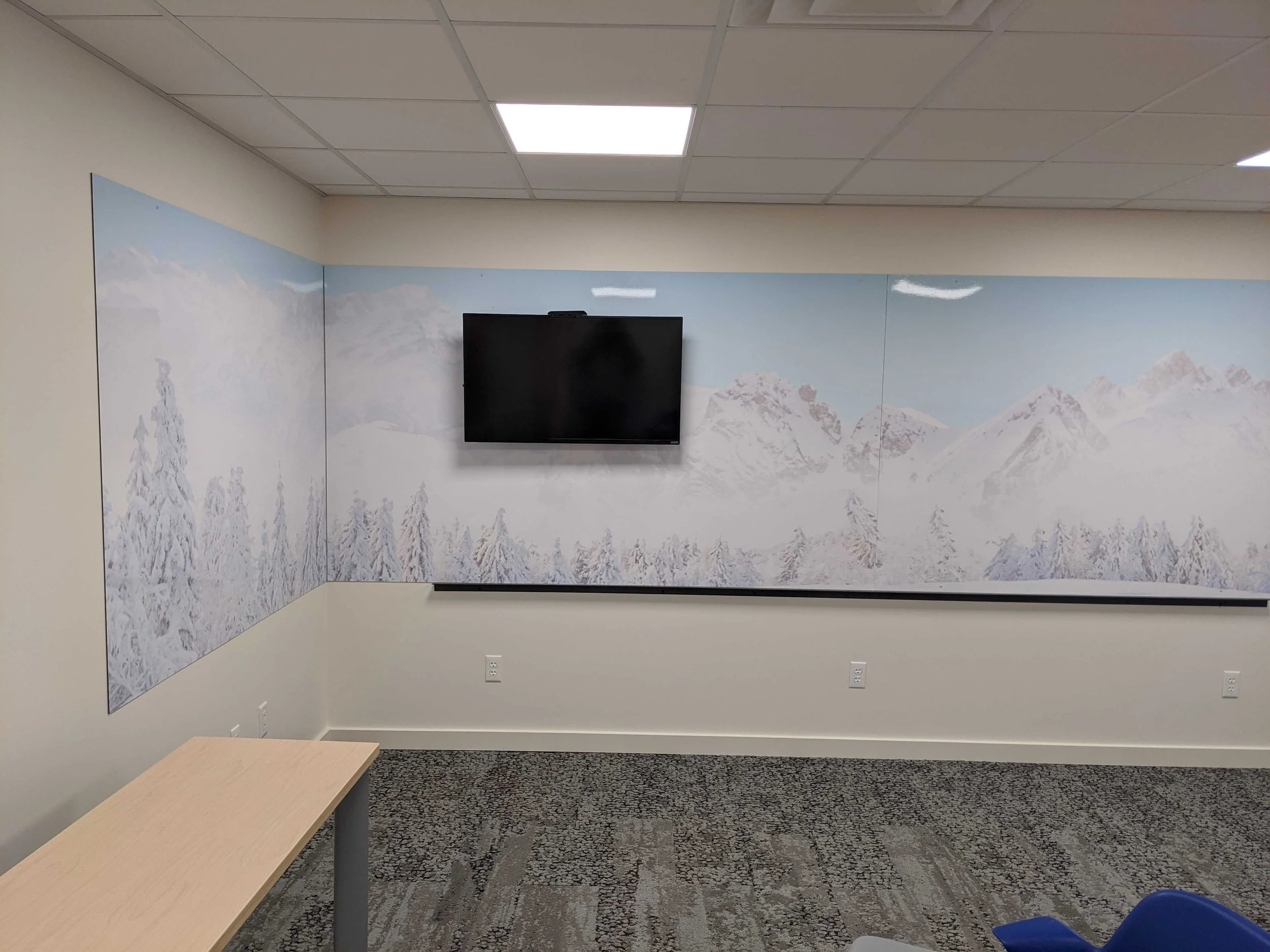 Snowy mountain dry erase wall wrap surrounding a mounted screen and continuing onto an adjacent wall.