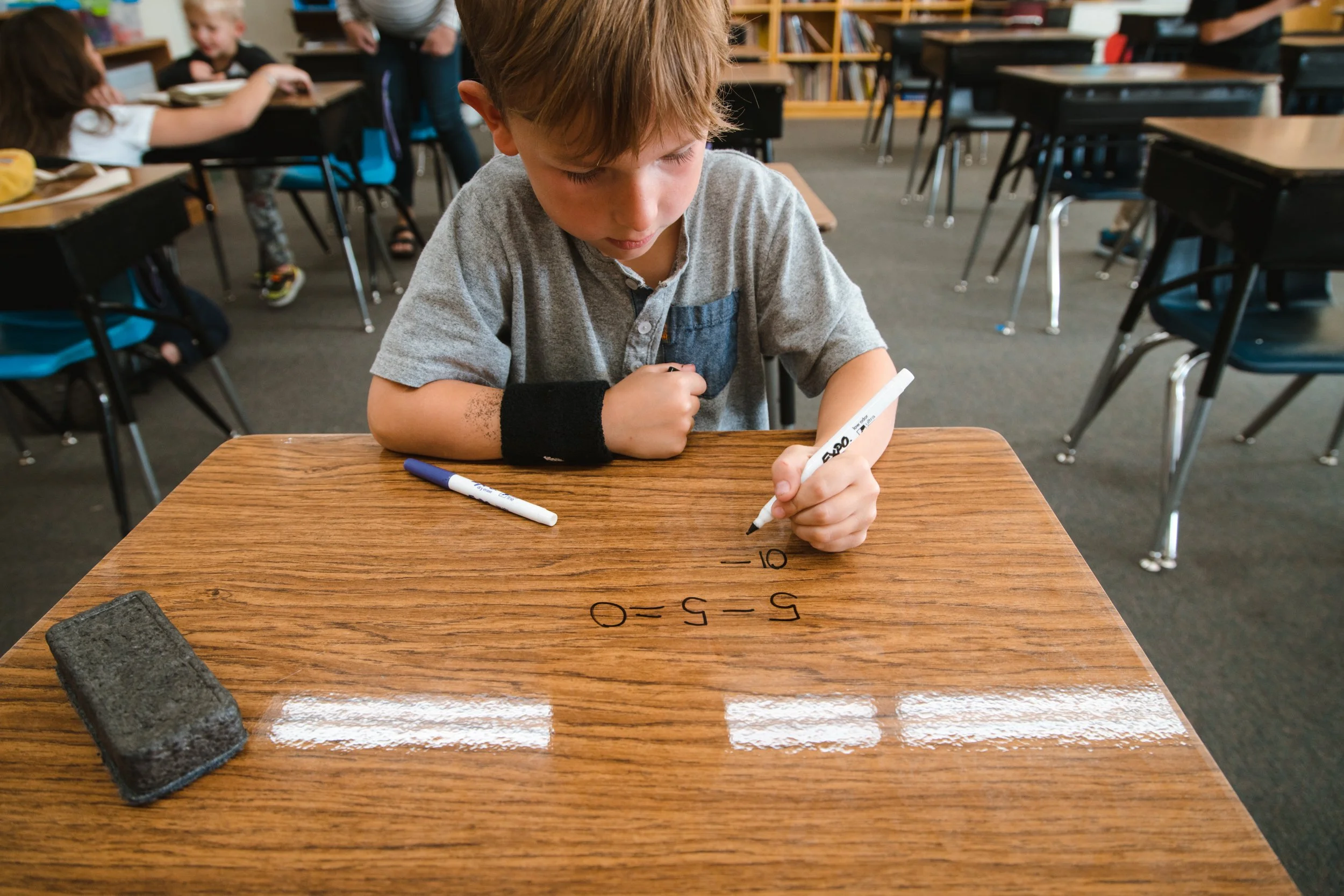 Student solving subtraction problems on a dry erase desk with markers and an eraser nearby.