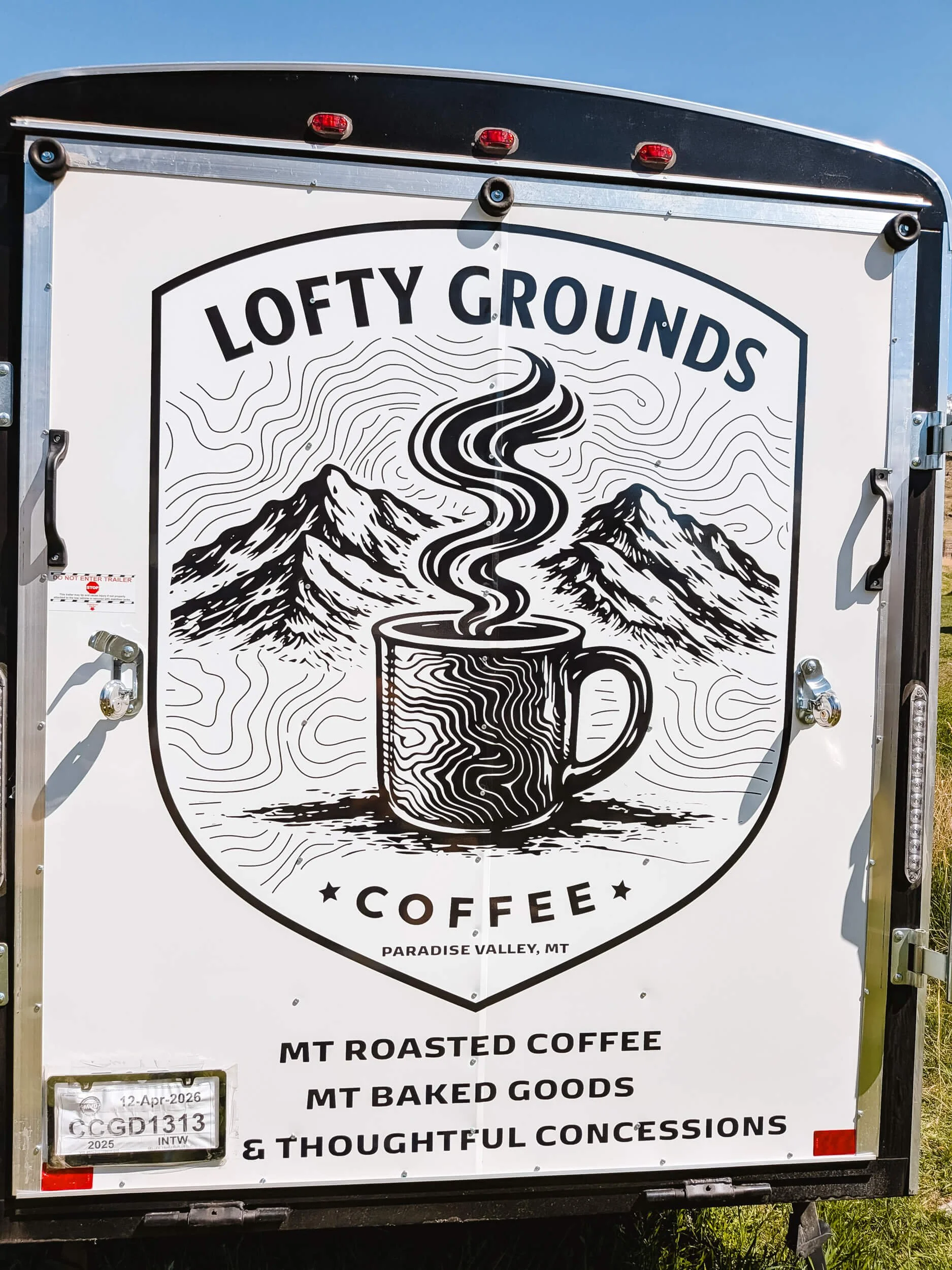 Shield-shaped logo on the back of a trailer featuring a steaming cup of coffee on a mountain and topo background
