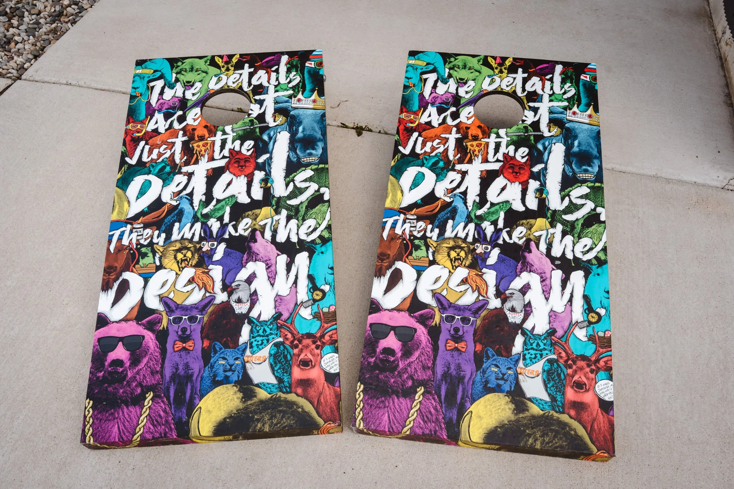 Matching cornhole boards covered in colorful custom vinyl wraps featuring illustrated animals and bold typography, exemplifying creative wrap applications for event or promotional games.