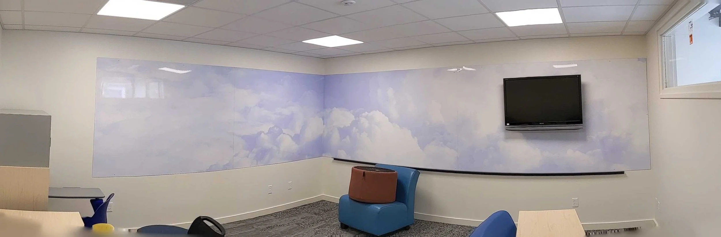 Panoramic view of cloud graphics on dry erase wall coverings with a screen mounted at one end.