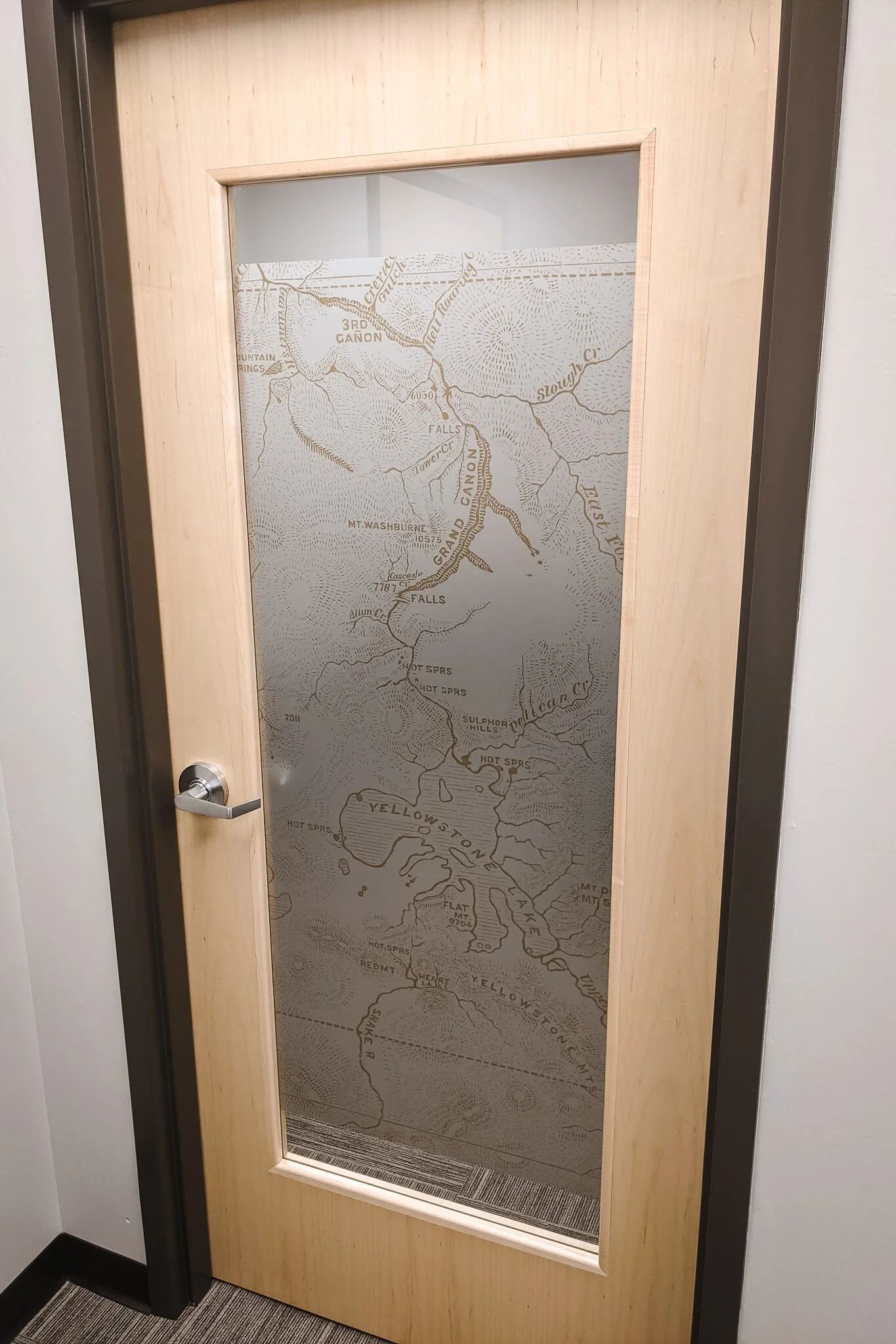 An interior office door with frosted window graphics displaying a detailed Yellowstone topographic map, applied to the glass panel for privacy while adding a custom branded design.