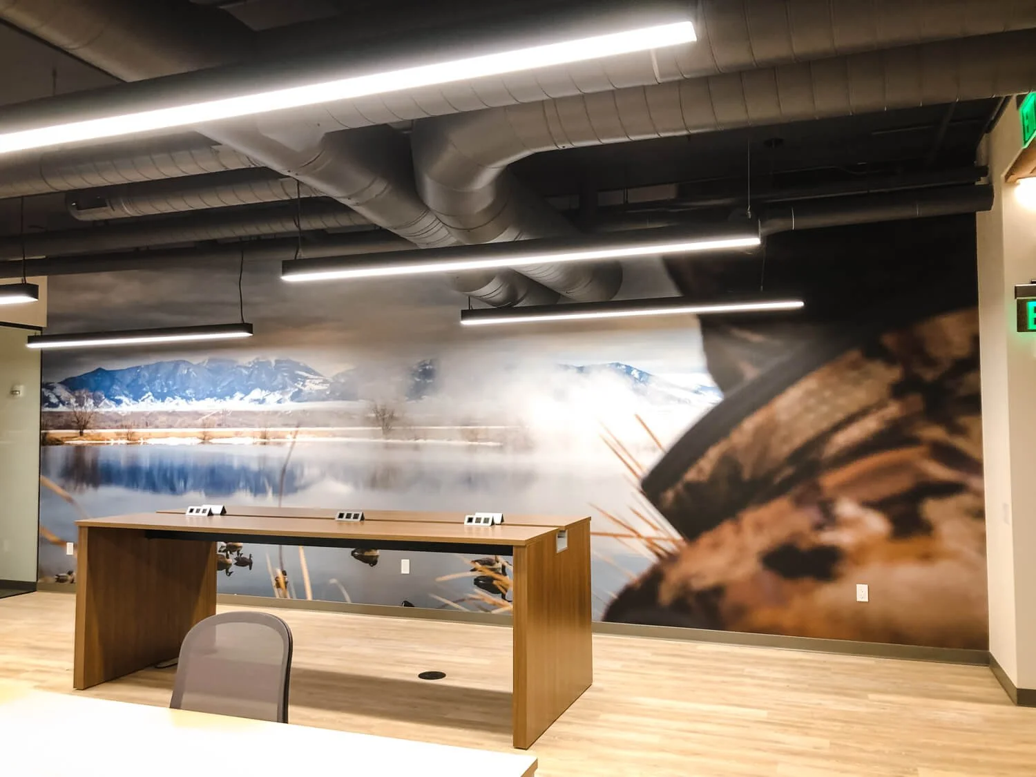 Custom scenic vinyl wall wrap featuring a lakeside view with snowcapped mountains and camo detailing, installed in a modern office with industrial lighting and exposed ductwork at Credova.