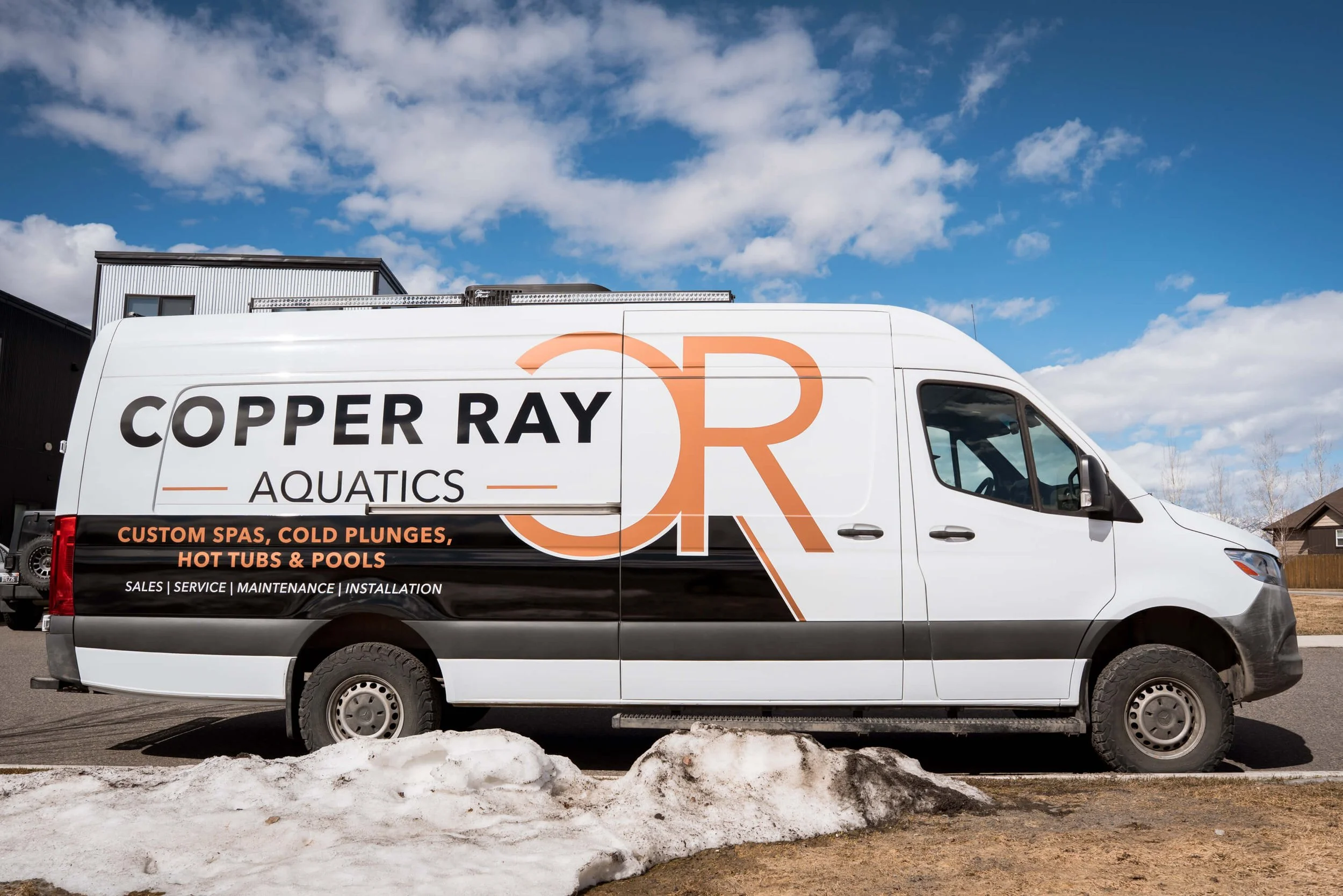 Full van wrap for Copper Ray Aquatics with large-scale logo, black and orange color blocking, and text for pool and spa services—an example of a branded fleet wrap for trades in Bozeman, Montana.