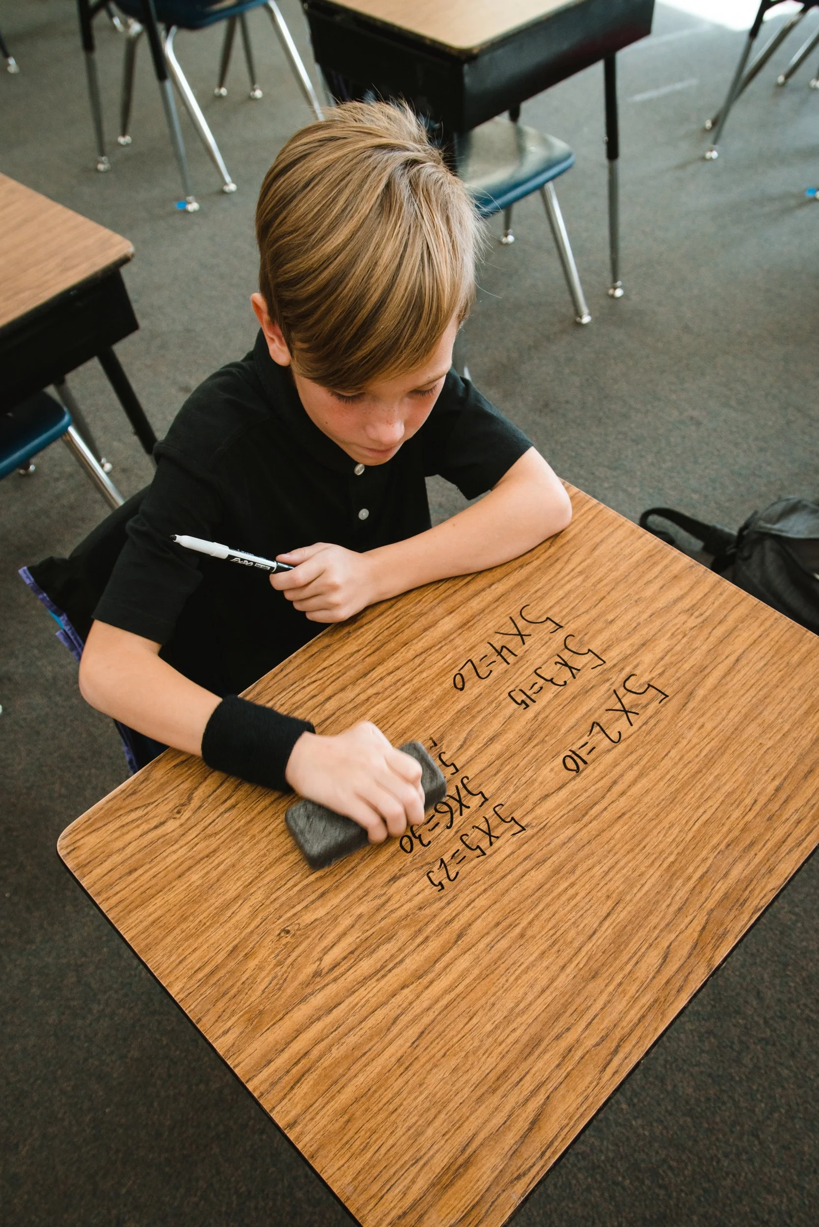 Student wiping away equations while holding a marker above a dry erase desk.