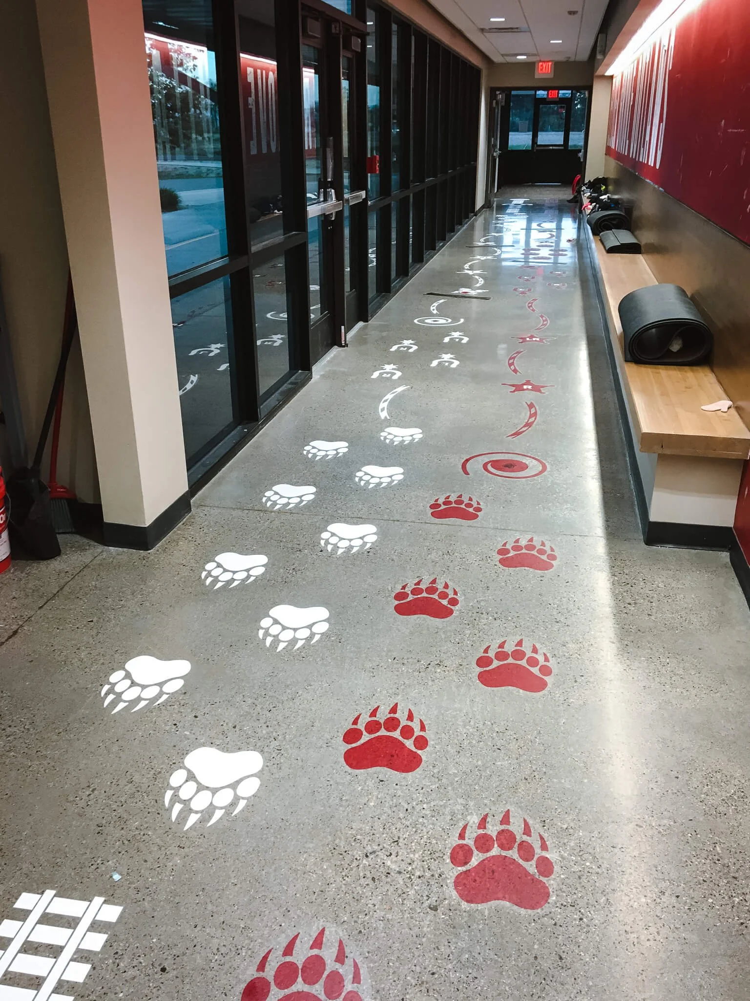 Hallway display featuring playful red and white bear paw prints and swirls applied with custom vinyl wraps to create an interactive path along a polished floor.