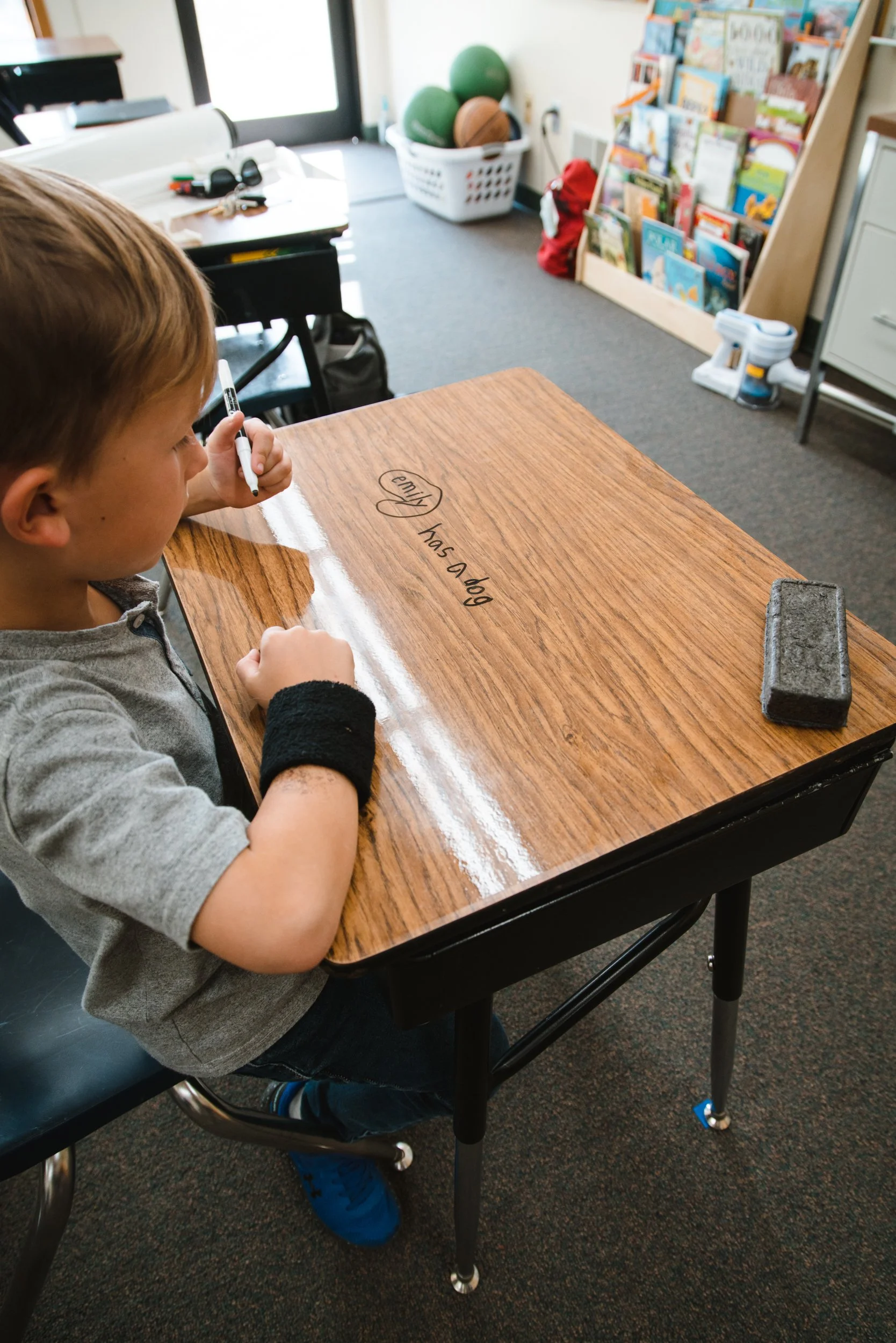 Side view of a student working on a woodgrain dry erase desk with a rectangular eraser nearby.