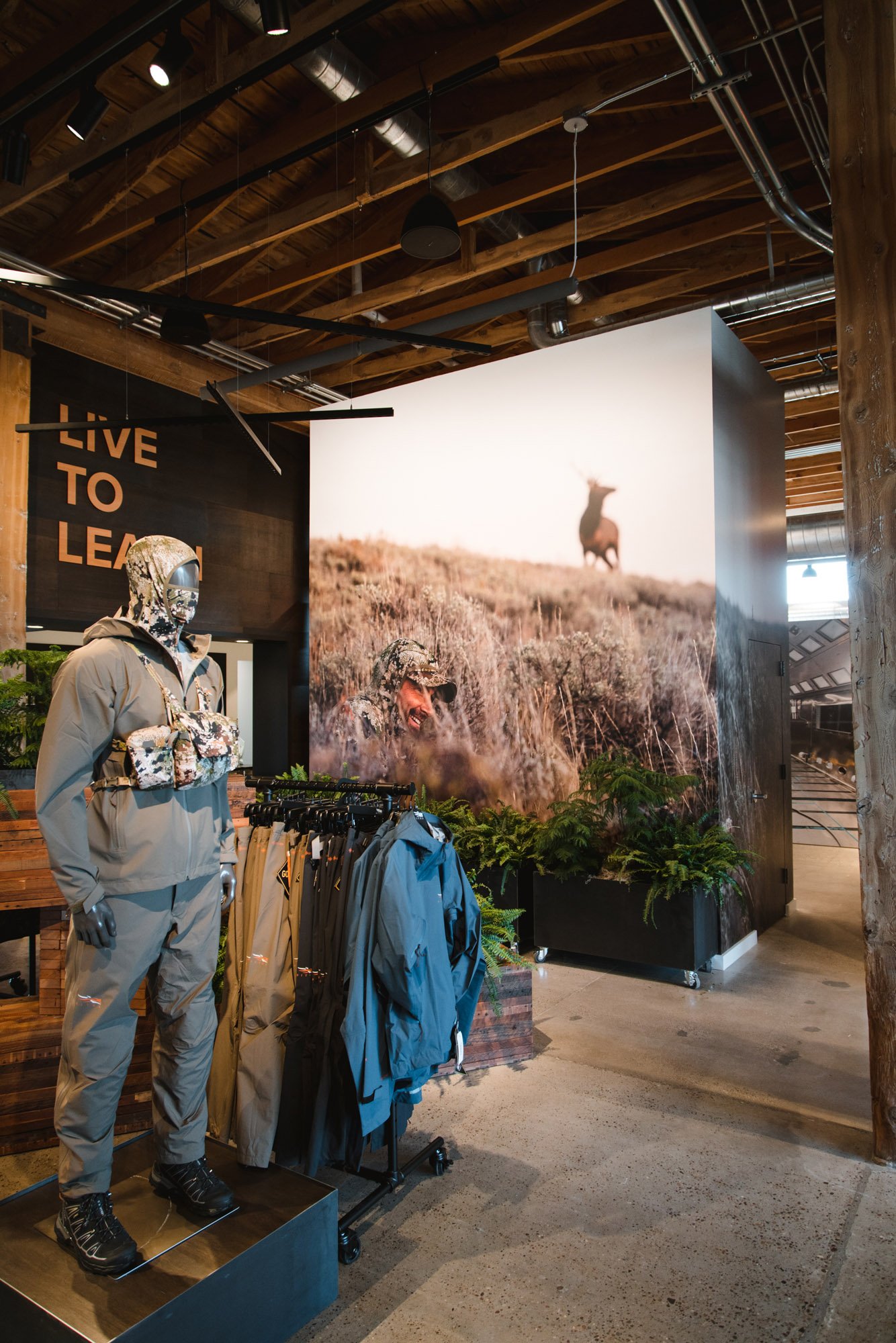 Photographic wall wrap showcasing a hunter in camouflage on a hillside with an elk in the background, featured in a high-ceiling commercial interior at Sitka Depot in Bozeman, MT.