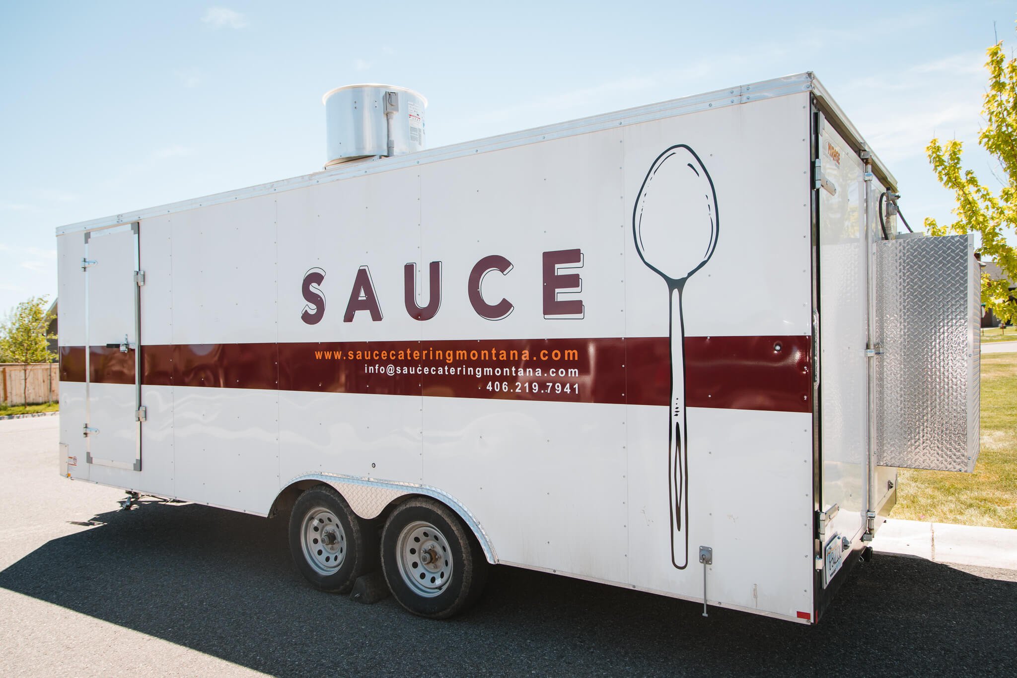 Trailer graphics for Sauce Catering Montana in Bozeman, Montana, with a clean white background, spoon illustration, and large maroon logo and website info.