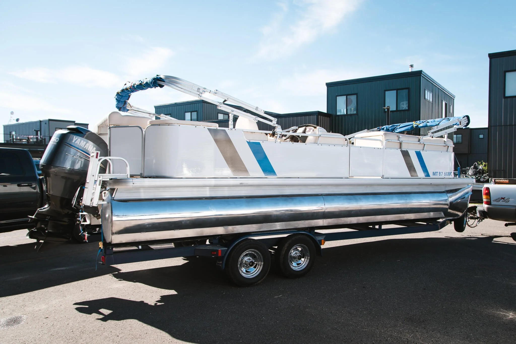 Pontoon boat with a subtle custom vinyl wrap in white and blue geometric accents, ready for the water and parked in a commercial lot in Bozeman, MT.