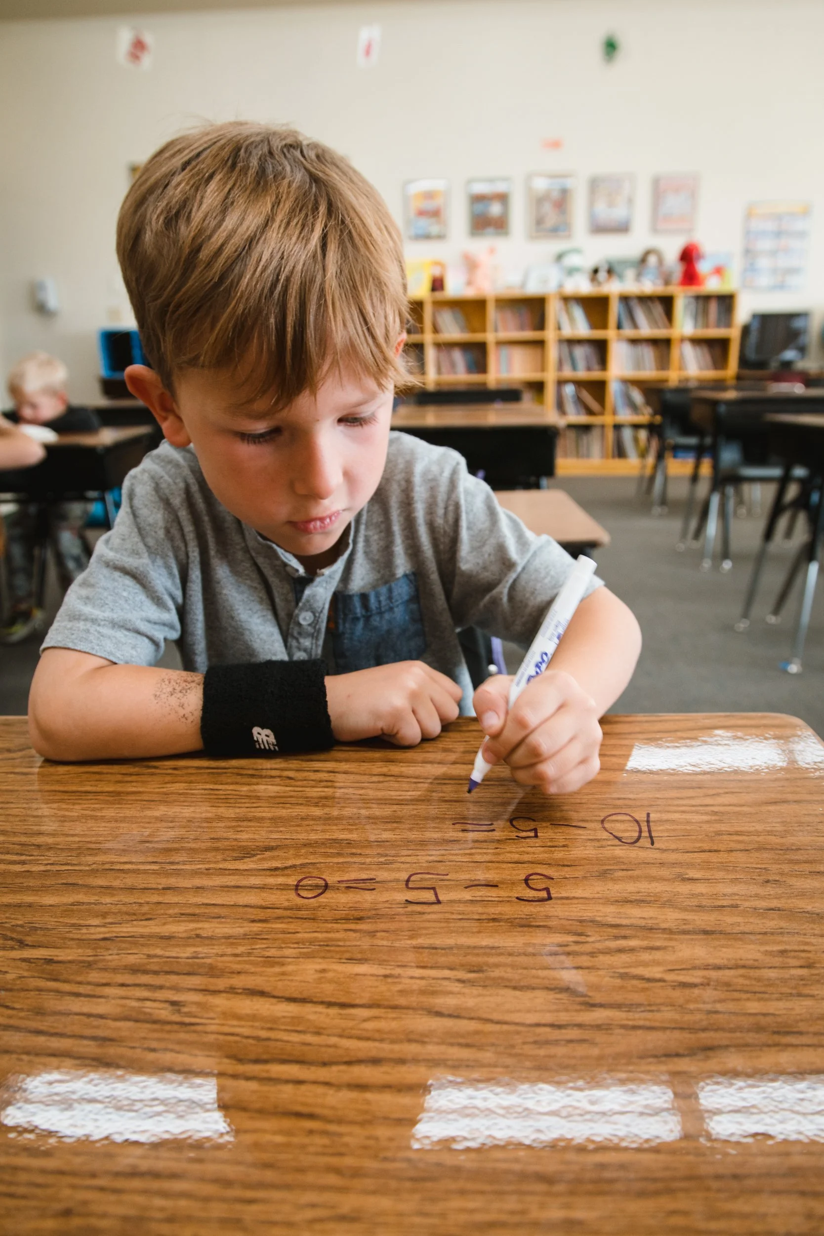 Student practicing subtraction on a glossy dry erase desk in a classroom.