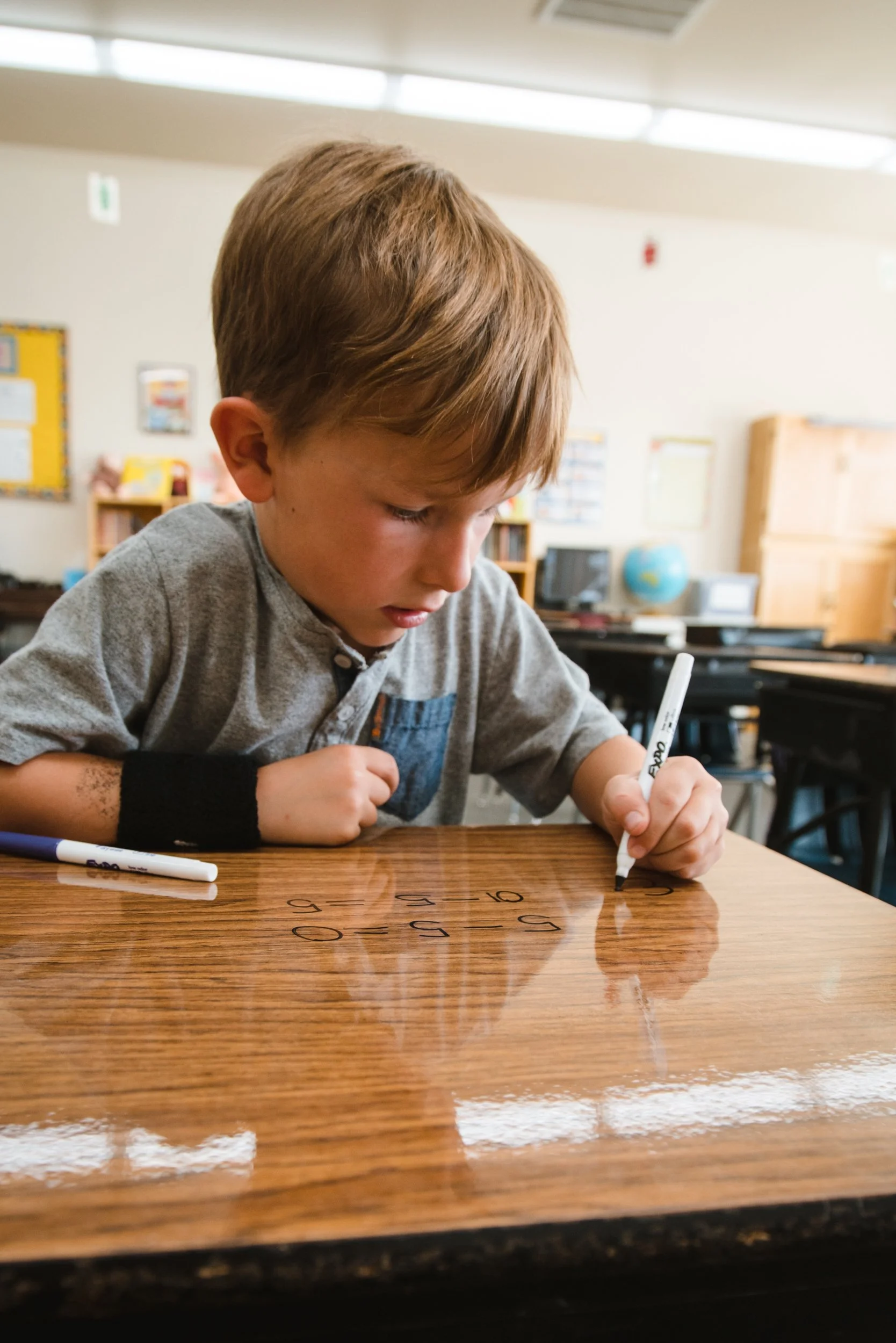 Close view of a student writing with black marker on a clear dry erase desk wrap.