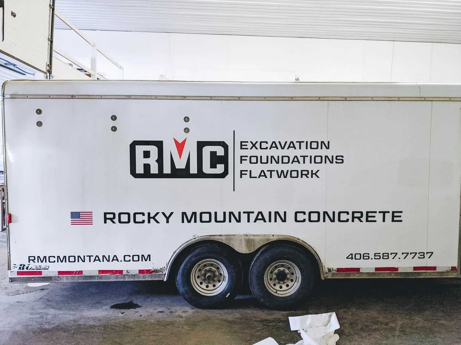 Rocky Mountain Concrete trailer wrap in Bozeman, Montana, featuring block lettering and a red-chevron RMC logo, highlighting excavation, foundations, and flatwork services on a white trailer.