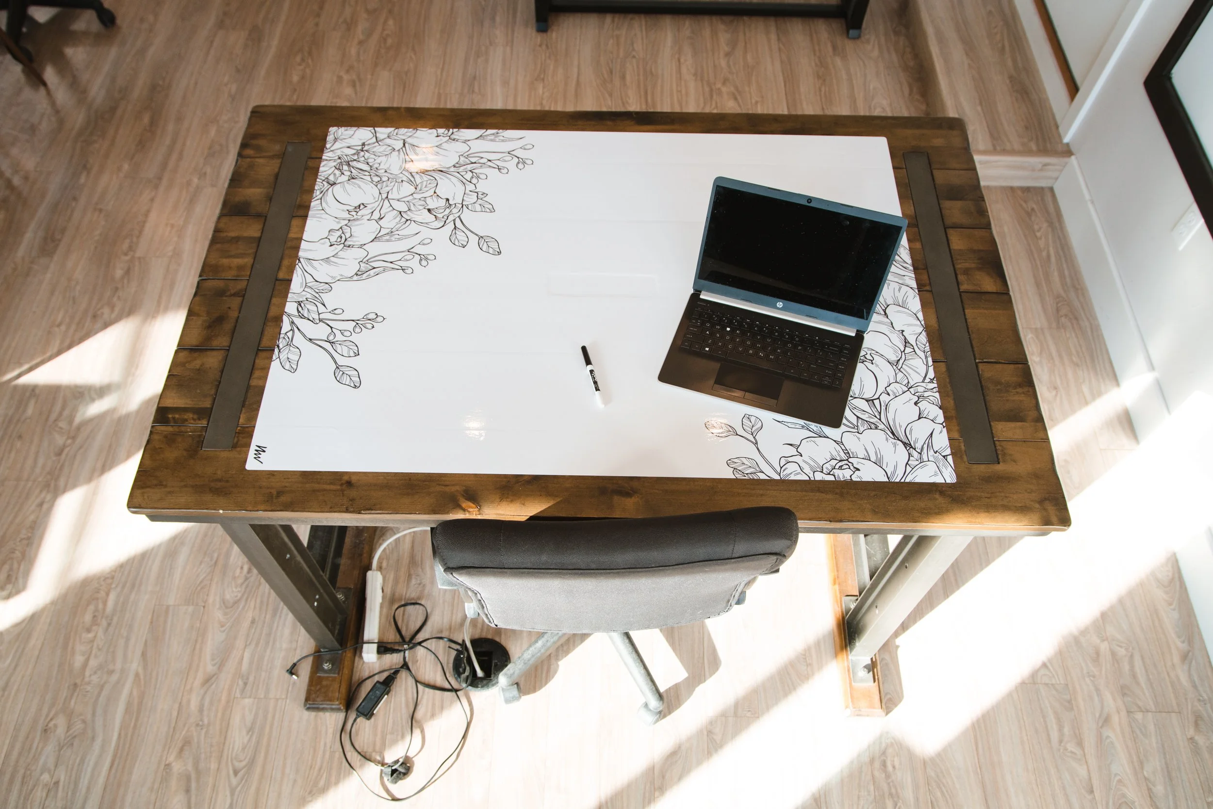 Overhead view of a wood desk with a floral dry erase wrap, laptop, and marker.