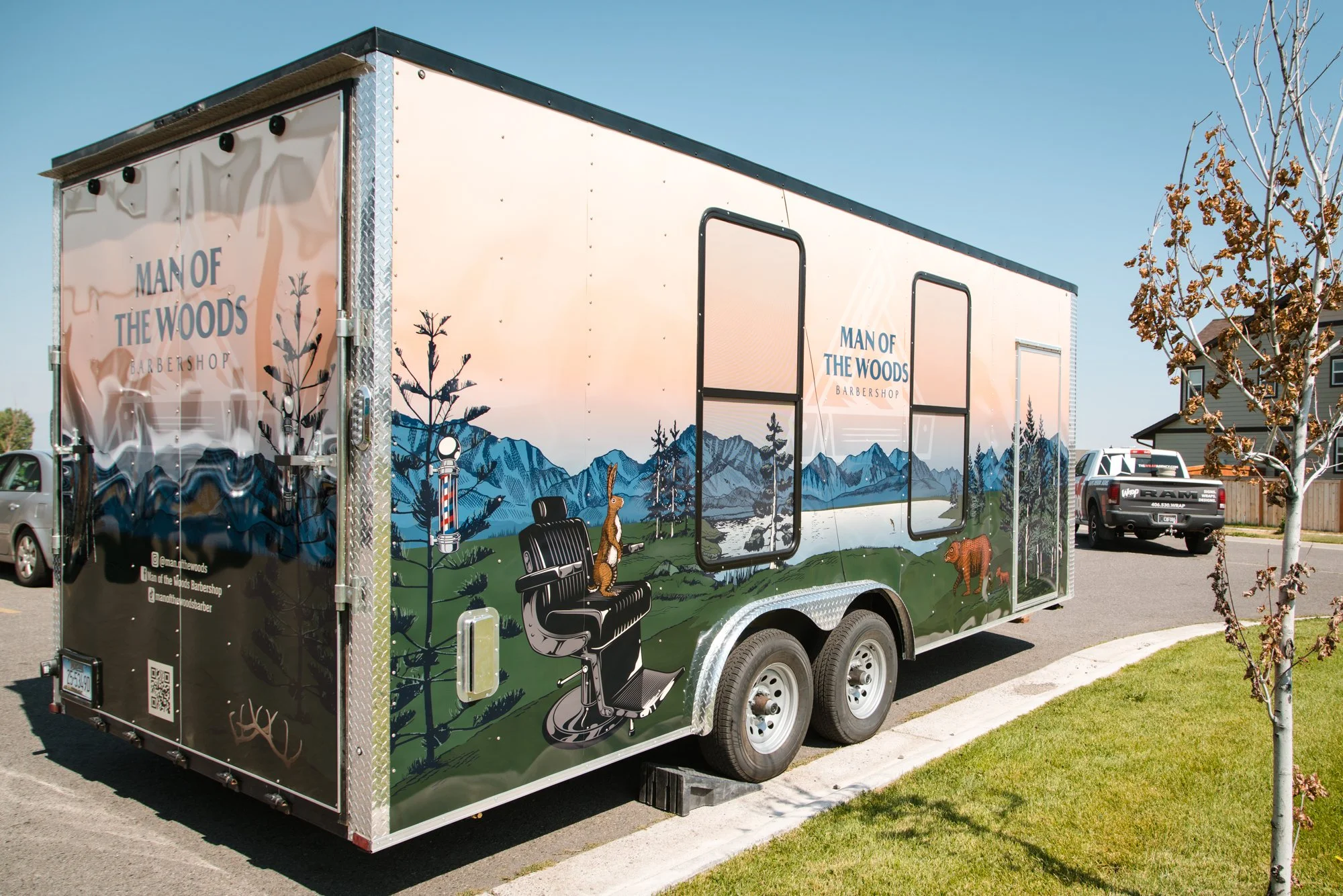 Mobile barbershop trailer with Man of the Woods branding, featuring mountain and forest graphics.