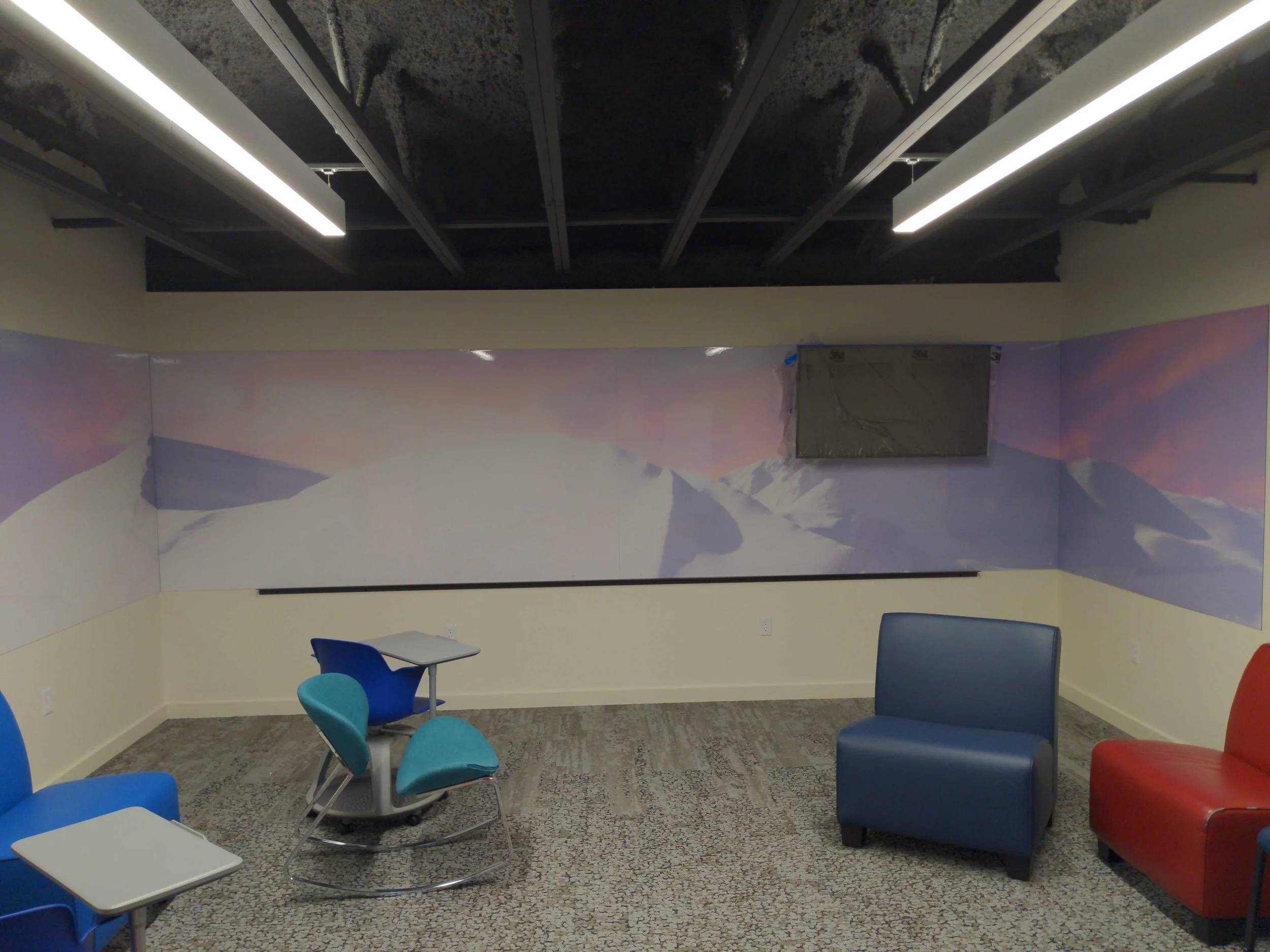 Mountain-themed dry erase wall graphics extending around a room beneath exposed ceiling beams.