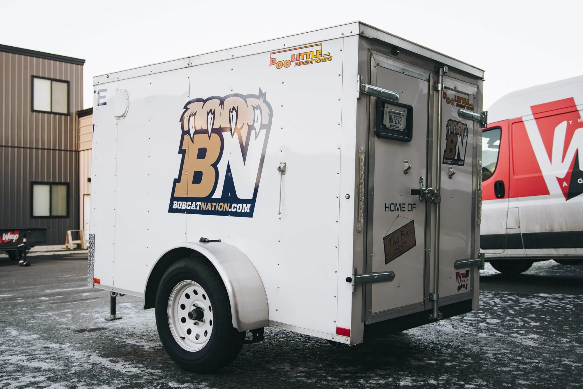 Exterior photo of a white Bobcat Nation trailer in Bozeman, Montana, with branded trailer graphics featuring the BN logo and website, used for sports team promotion and mobile marketing.