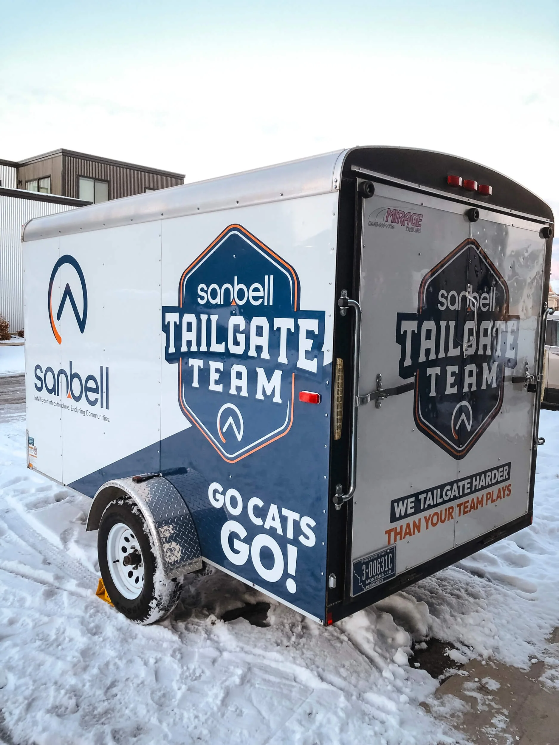 Sanbell Tailgate Team vinyl graphics on a small white trailer. Graphics are navy blue and orange