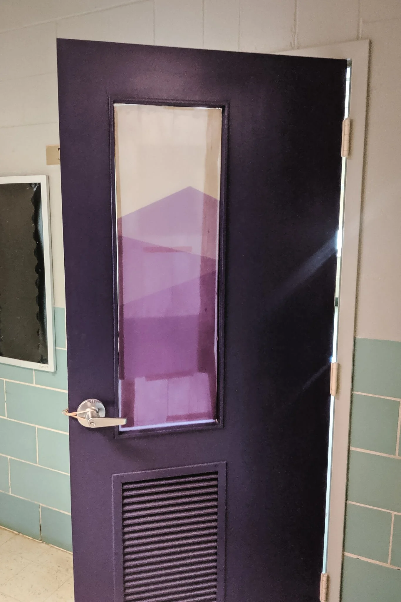An interior door painted purple with a narrow glass window featuring layered geometric window graphics in translucent purple shades, designed for privacy while allowing light through.