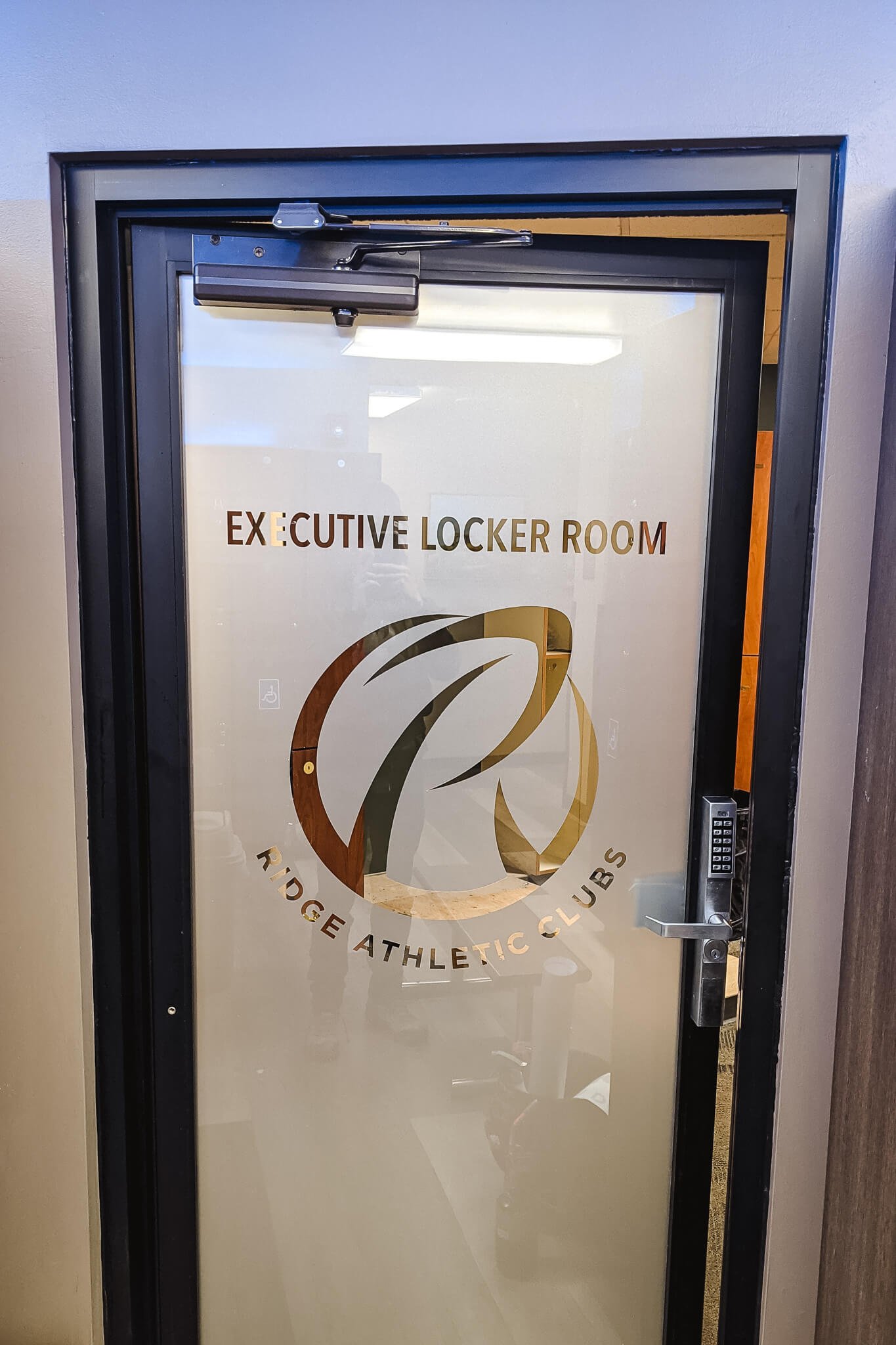 Etched glass-style door graphics display the Ridge Athletic Clubs logo and “Executive Locker Room” text in a sleek, modern fitness facility.