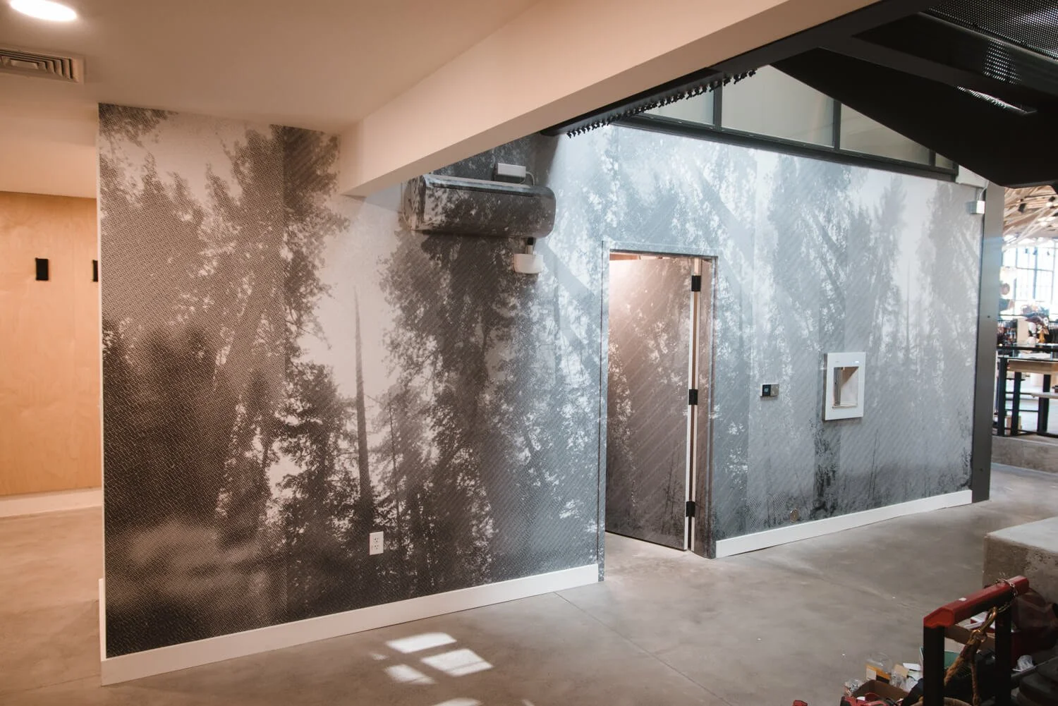 Monochrome forest scene wall wrap installed on angular surfaces with integrated vents and doors, adding texture and depth to a modern industrial commercial space at Backcountry in Bozeman, MT.