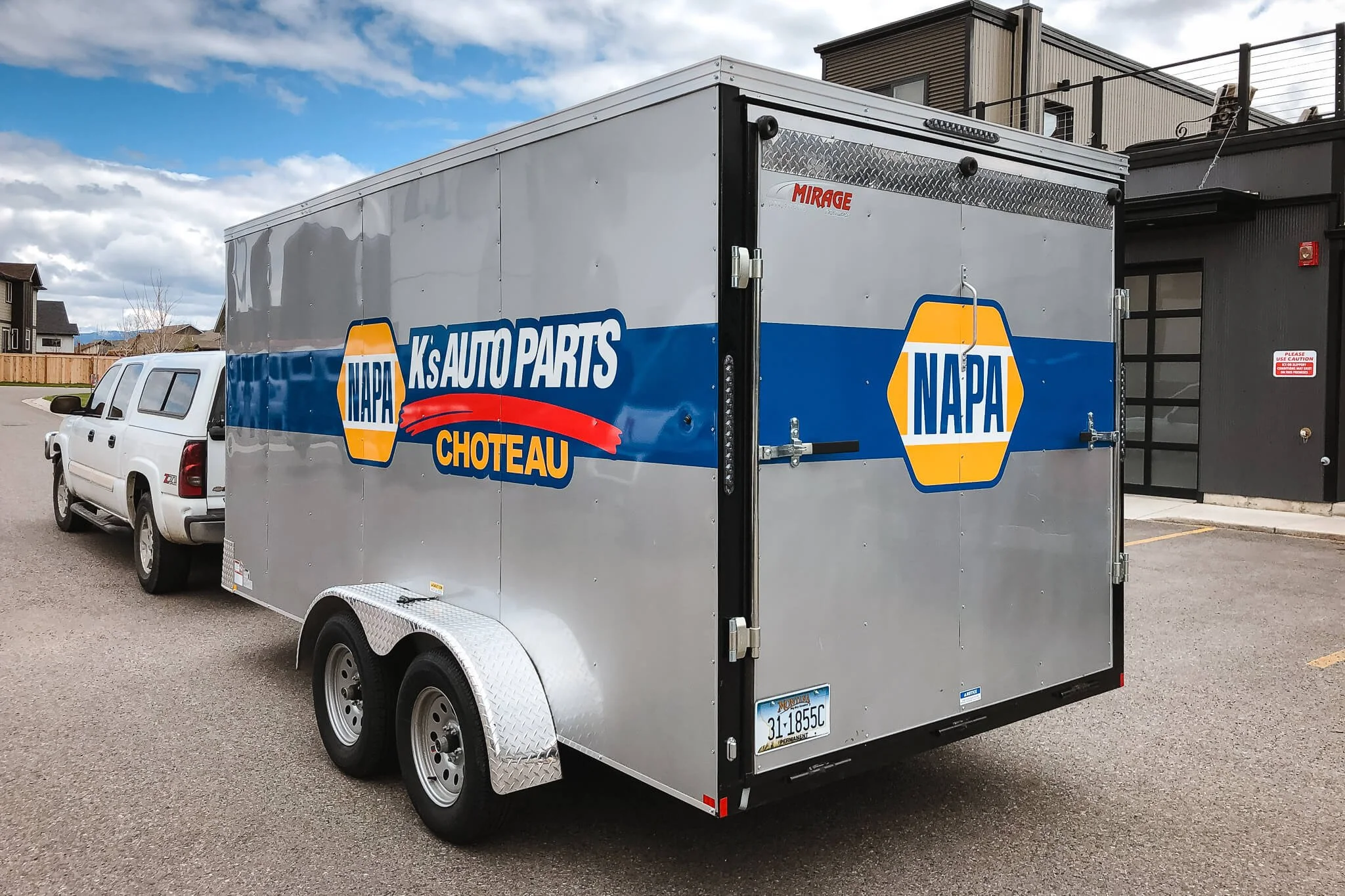 Side view of a silver NAPA Auto Parts trailer in Bozeman, Montana with branded trailer graphics for K’s Auto Parts Choteau, including the NAPA logo, blue and red design elements.
