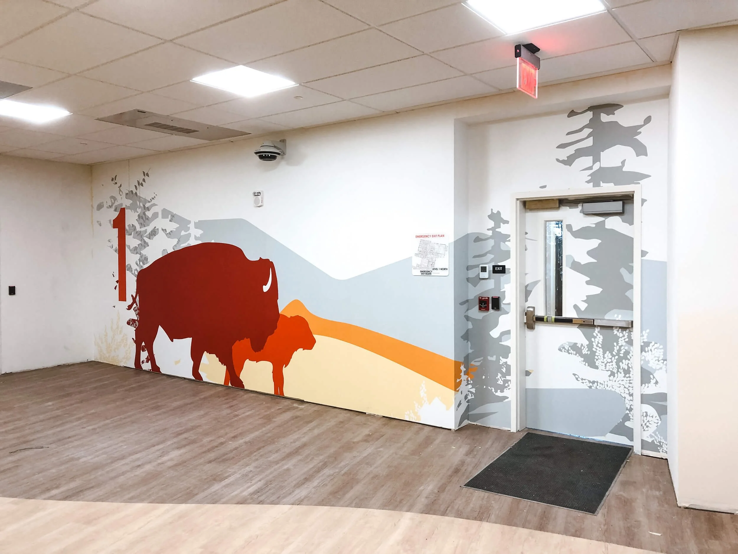 Nature-inspired wall wrap with a bison and calf silhouette beside a bold red number 1, set in a clinical or educational hallway to indicate floor or zone number. Installed at Shodair Children’s Hospital in Helena, MT.