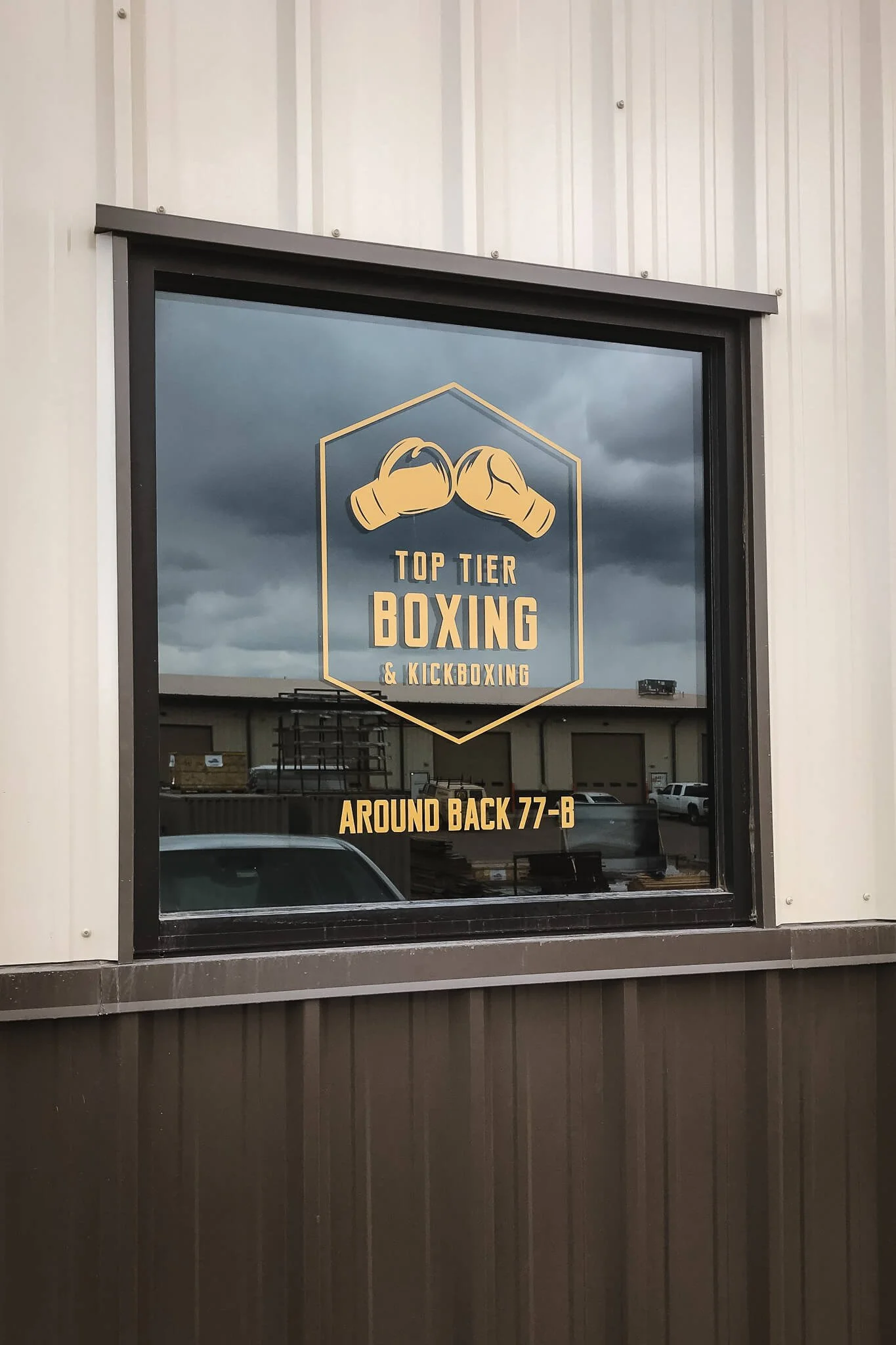 Custom-cut yellow vinyl window graphic with boxing gloves and text for Top Tier Boxing & Kickboxing in Bozeman, MT, applied to a dark reflective storefront window.