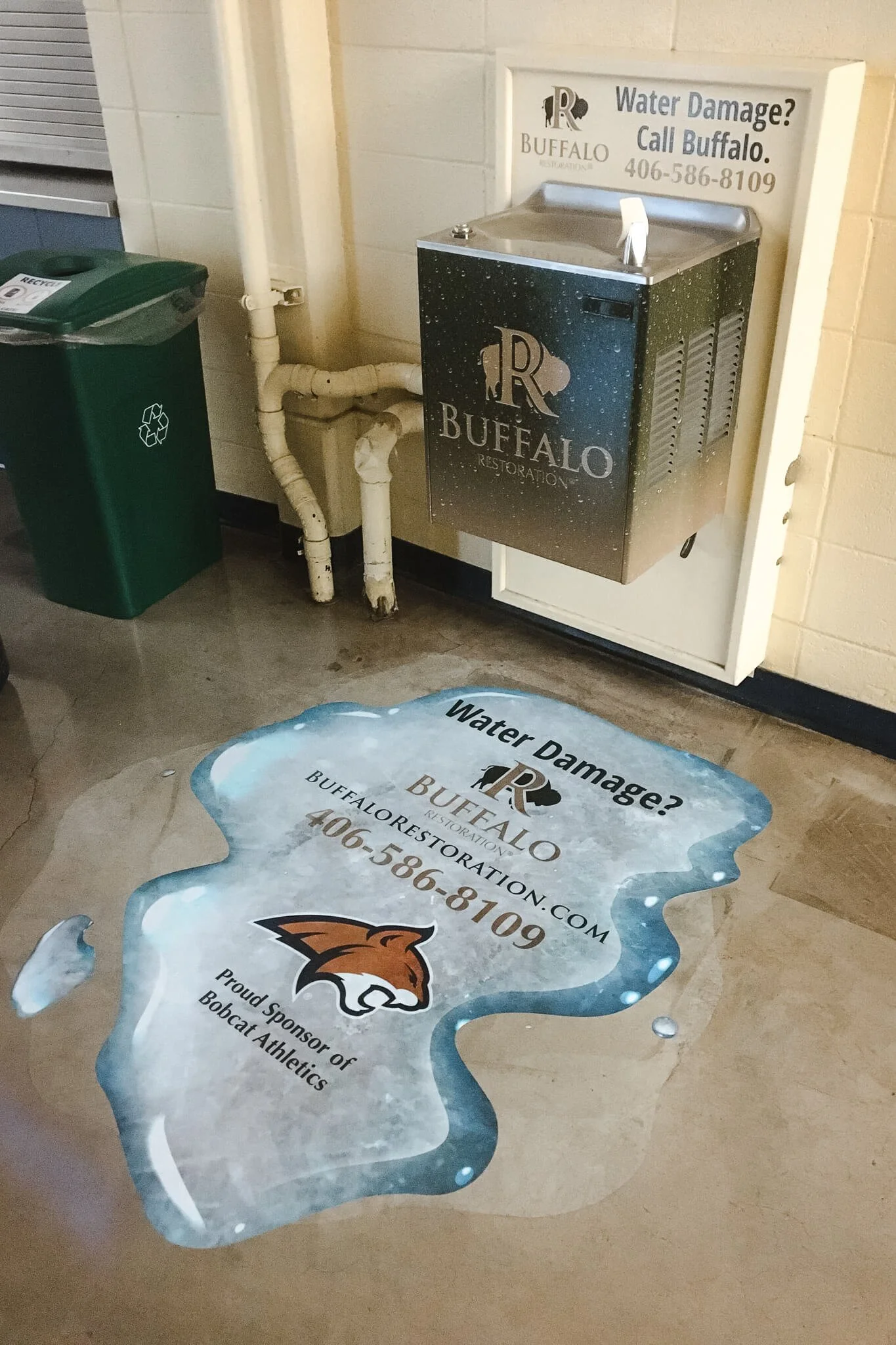 Realistic 3D-style floor vinyl designed to look like a water puddle next to a drinking fountain, printed with custom vinyl wraps for Buffalo Restoration’s branding.