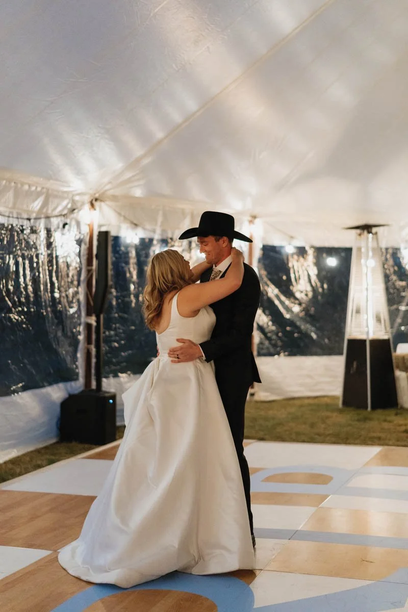 Bride and groom share their first dance on a monogrammed vinyl dance floor wrap at 320 Guest Ranch in Montana. Custom wedding graphic installed by Golden Hour Events. Photo by Danielle Mullens Photography.