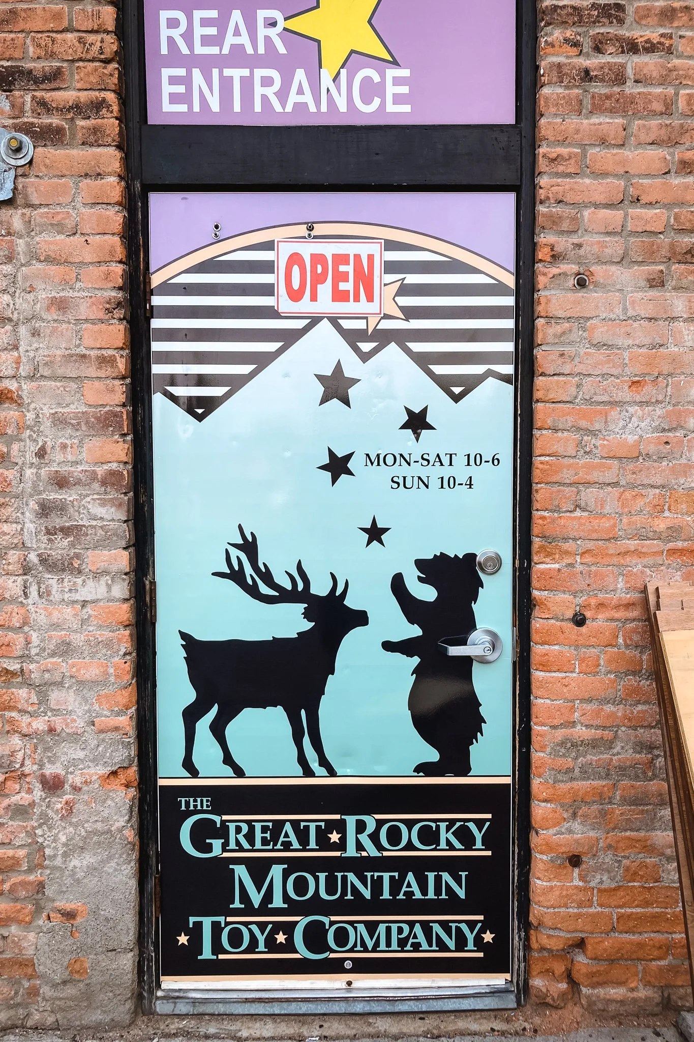 Vibrant storefront door wrap featuring silhouettes of a reindeer and a child reaching for stars, along with the business name “The Great Rocky Mountain Toy Company” on a brick exterior in Bozeman, MT.